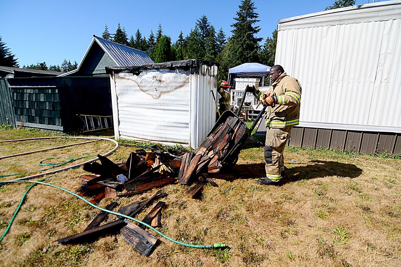 East Jefferson Fire-Rescue firefighter DeAndrew Wesley overhauls an outbuilding that caught fire in Olympic Trailer Park near Port Townsend on Tuesday. (Jesse Major/Peninsula Daily News)