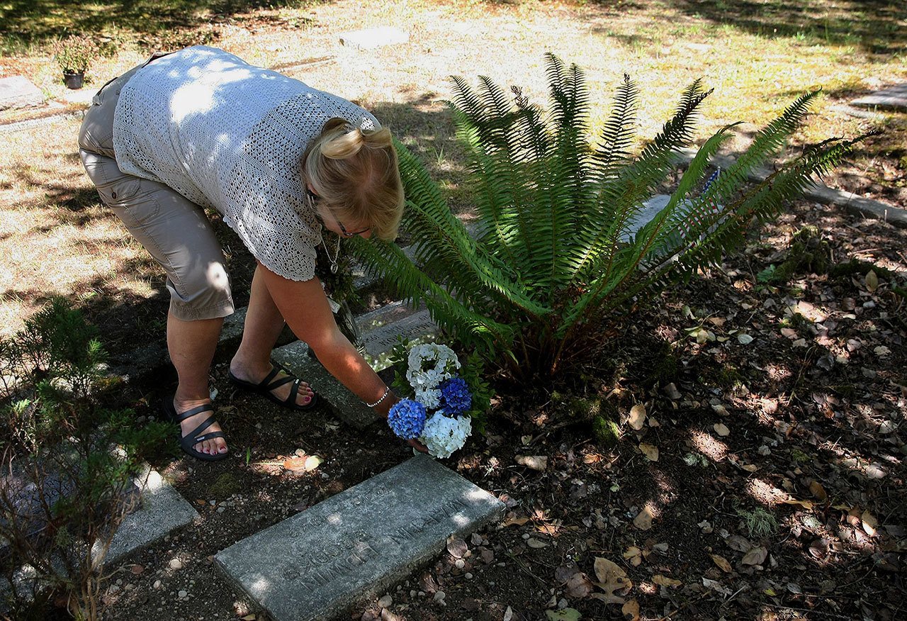 Joanne Clark, the secretary/treasurer for the Fraola Cemetery, places a fresh flower vase at a marker for Martin Edwin Brooks at the cemetery in Olalla on Aug. 5. The marker was found by the side of the road in Lewis County. (Larry Steagall/Kitsap Sun via AP)