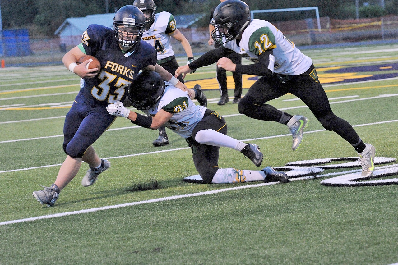 Lonnie Archibald/for Peninsula Daily News Forks’ Tristian Pisani (33) attempts to avoid the tackles of Vashon’s Sol Dehnert (21) and Conner Hoisington.