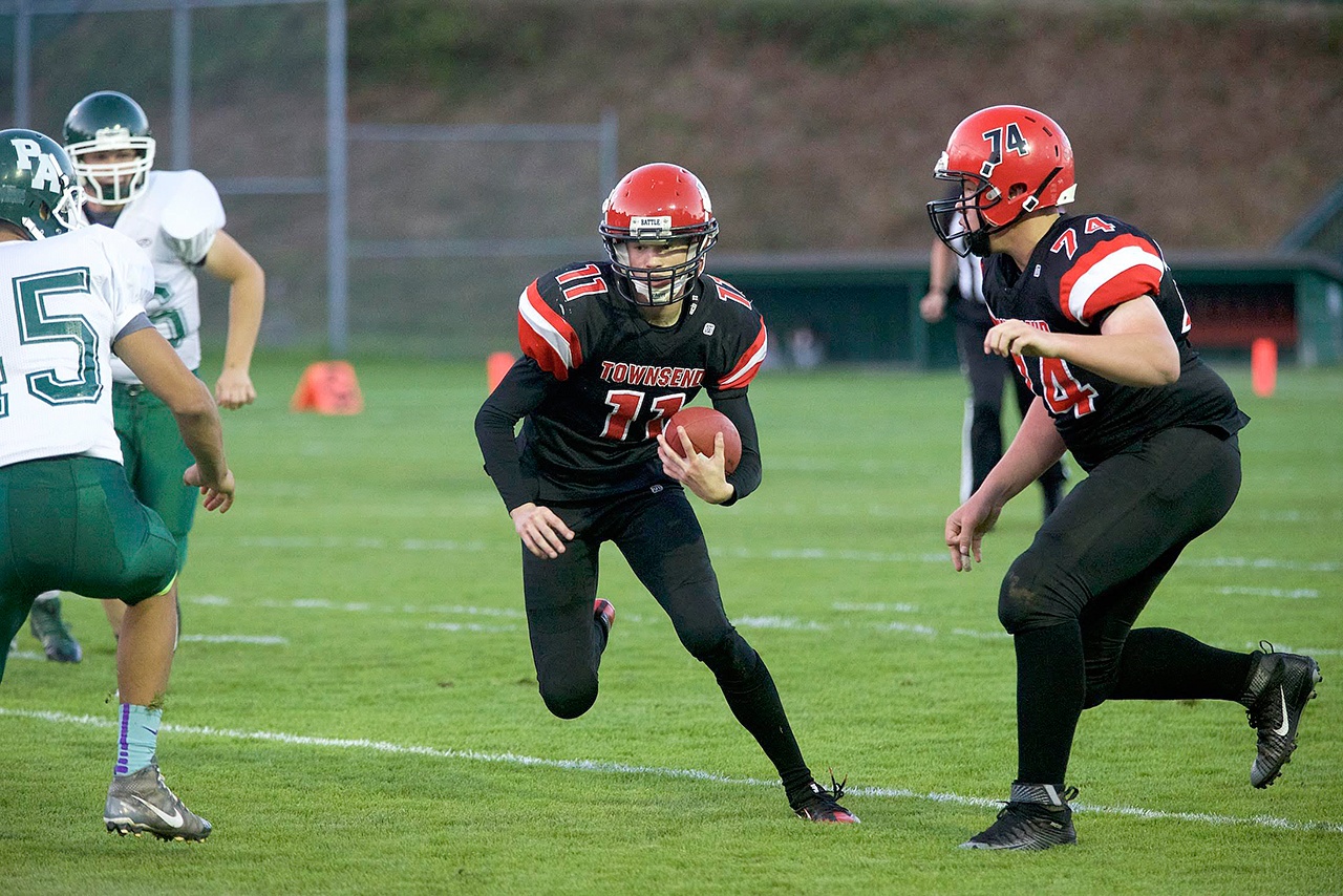 Steve Mullensky/for Peninsula Daily News                                Port Townsend ‘s Berkley Hill plants a foot and dodges the tackles of a pair of Roughriders during a game played in Port Townsend on Thursday. Jackson Foster, 74, is ready to assist in the play.