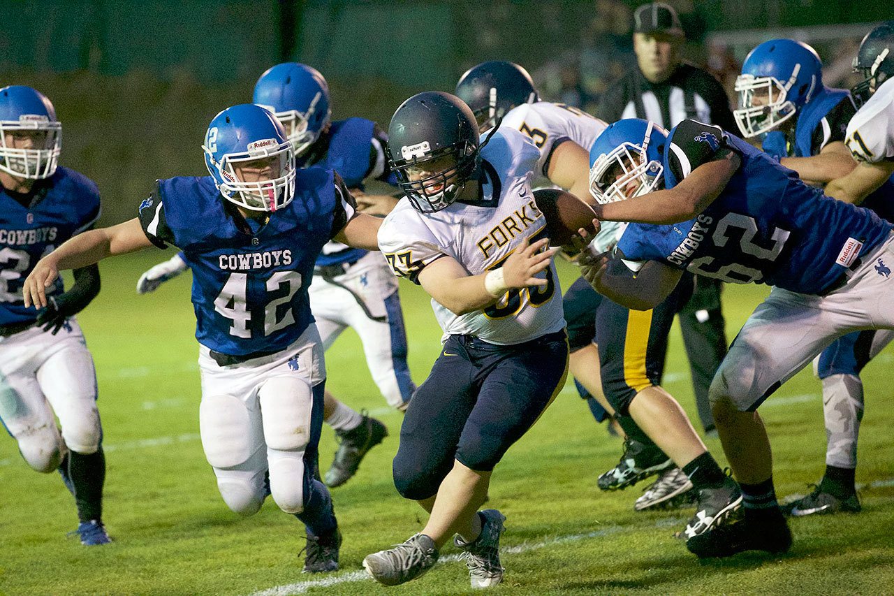 Steve Mullensky/for Peninsula Daily News Forks’ Tristen Pisani rushes for yardage while being chased by a posse of Chimacum Cowboys,Elijah Avery, 42, and Owen Brummell, 62, during a game Friday at Memorial Field in Port Townsend.