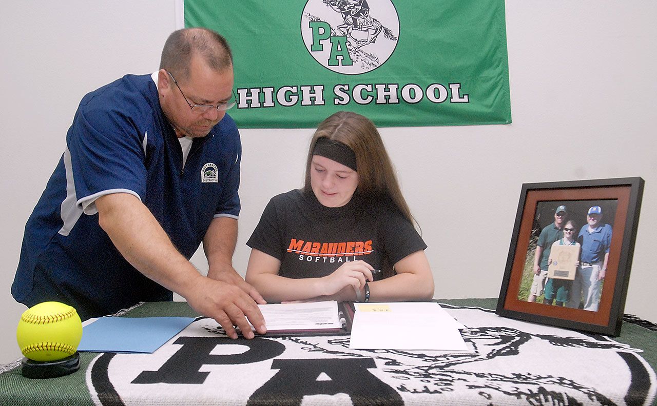 Keith Thorpe/Peninsula Daily News                                Port Angeles High School senior Lauren Lunt, seated, goes over paperwork with athletic director Dwayne Johnson prior to Lunt’s signing of a letter of intent on Friday to attend University of Mary in Bismarck, N.D., on a softball scholarship. A portrait of her, her father, Jeff Lunt, and grandfather, Jim Lunt, was displayed on the table.