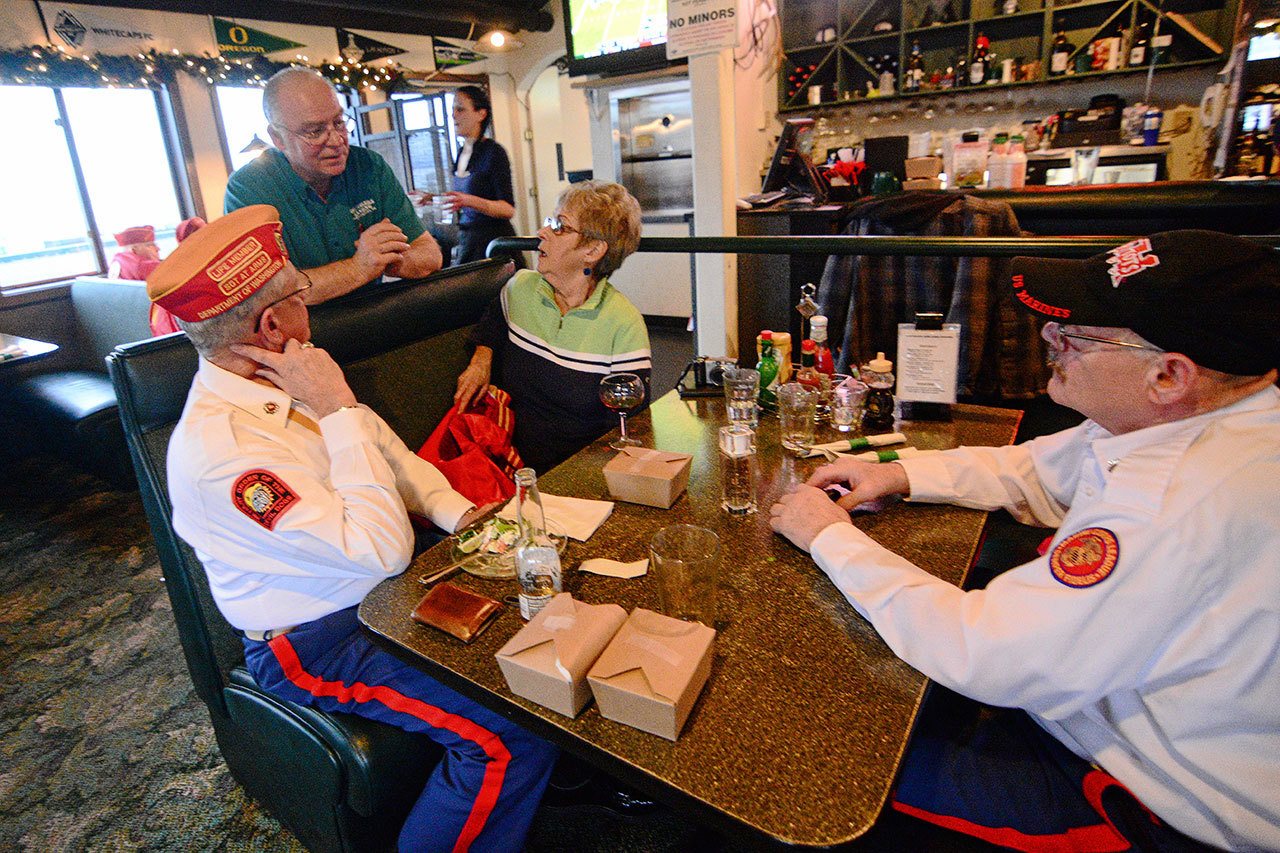 Marine Corps veterans Mark Schildknecht, front left, and Guy Iredale, right, chat with Smuggler’s Landing owner Rick Mathis after the free meal he gave veterans last week. (Jesse Major/Peninsula Daily News)