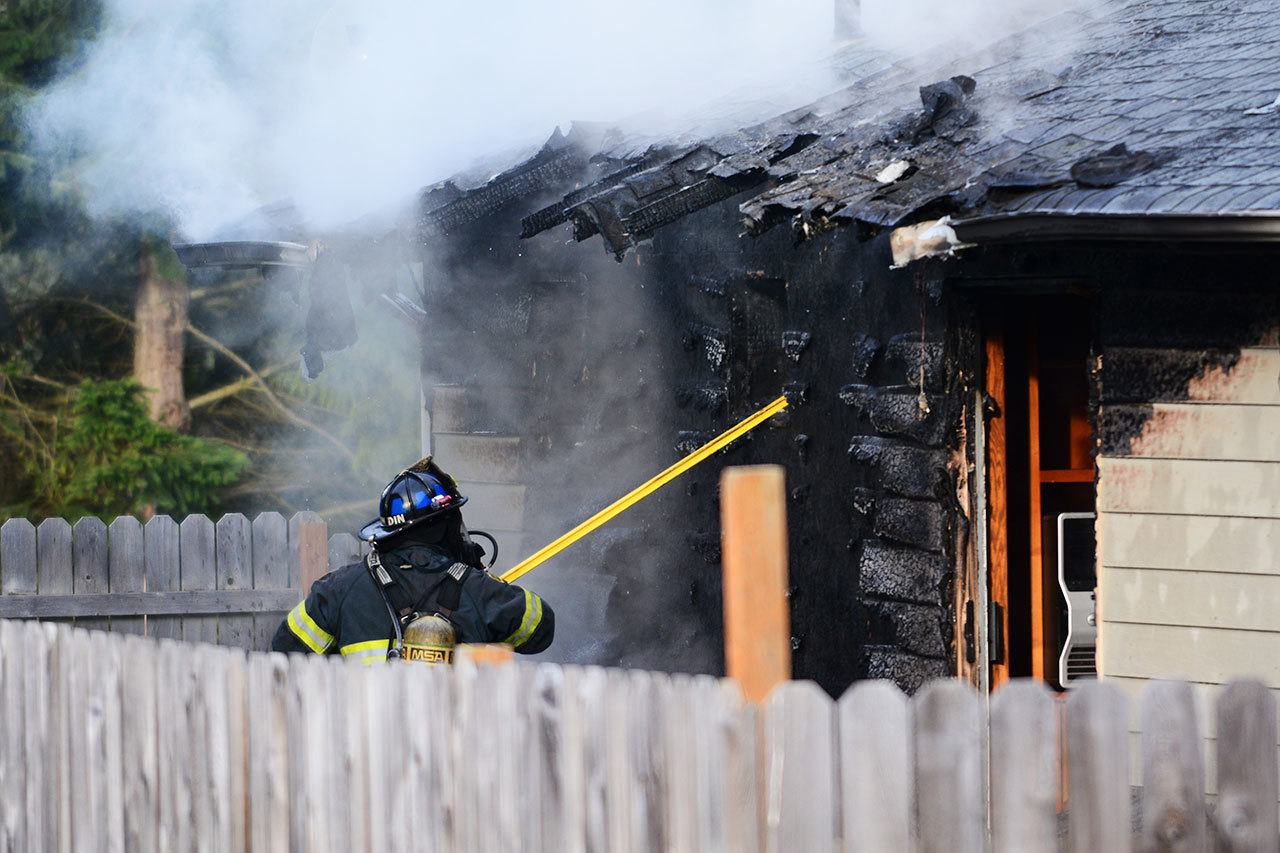 A firefighter overhauls a house on the west side of Port Angeles that caught fire Sunday morning. (Jesse Major/Peninsula Daily News)
