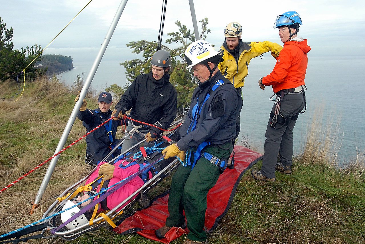 Katie Babcock, a member of the Clallam County Search and Rescue team, in litter, volunteers to be a victim during a rescue drill Wednesday on a waterside slope at the former Clallam County landfill in Port Angeles. Taking the role of rescuers were, from left, Kjel Skov of the Clallam County Fire District No. 3 rescue team, Troy Treaccar of Olympic Mountain Rescue, Mike Sprenger of Fire District No. 3, Kyle Pease of Olympic Mountain Rescue and Kelly Thomas of Clallam Search and Rescue. (Keith Thorpe/Peninsula Daily News)