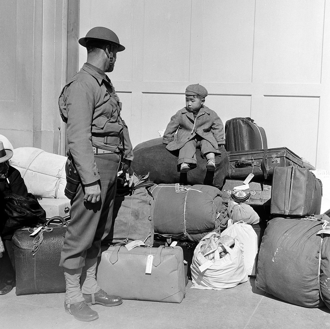 In this April 6, 1942, photo, a boy sits on a pile of baggage as he waits for his parents, as a military policeman watches in San Francisco. More than 650 citizens of Japanese ancestry were evacuated from their homes and sent to Santa Anita racetrack, an assembly center for war relocation of alien and American-born Japanese civilians. (The Associated Press)