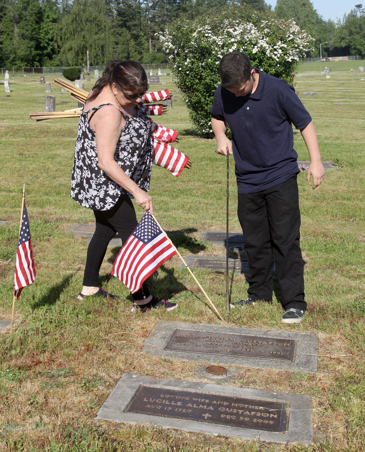 Linda Uhlig and her grandson Jason Kibe, 13, of Port Angeles place an American flag near the grave of a fallen military hero at Ocean View Cemetery in Port Angeles. (Dave Logan/for Peninsula Daily News)