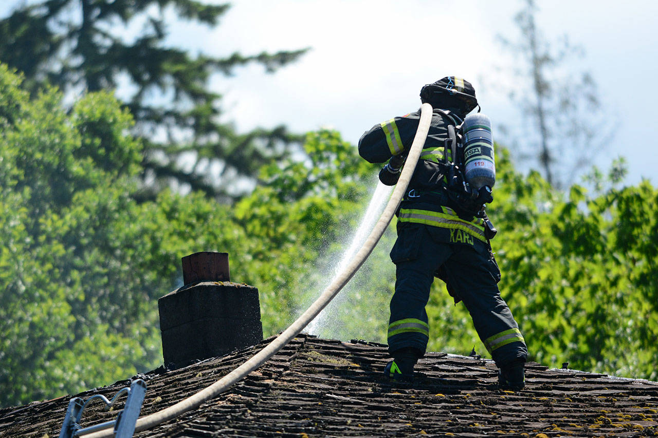 Port Angeles firefighter Mark Karjalainen sprays down the roof of a Port Angeles home that caught fire Sunday afternoon. (Jesse Major/Peninsula Daily News)