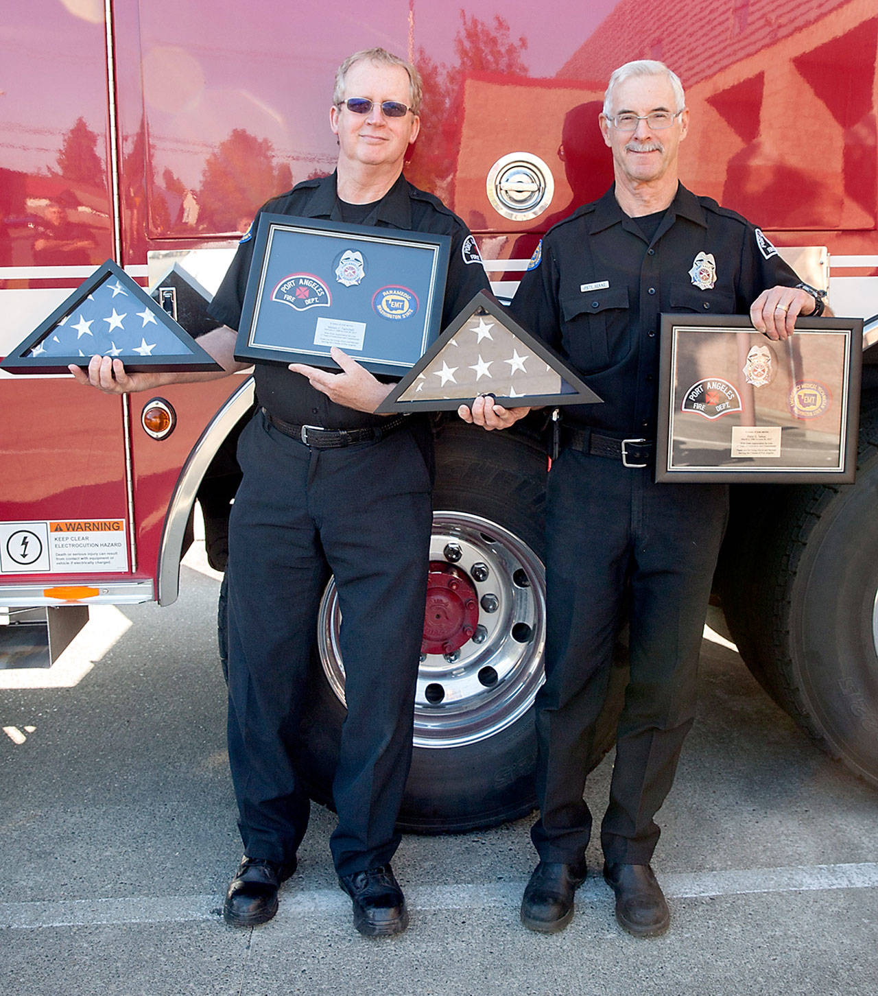 Port Angeles firefighters Mel Twitchell, left, and Pete Sekac, right, were honored with flags at their retirement ceremony Friday morning. (Patti Reifenstahl)