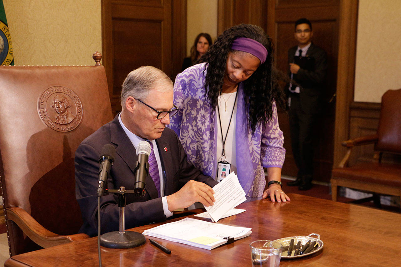 Gov. Jay Inslee reads veto messages while legislative assistant Angie Adams looks on Friday in Olympia. (Rachel La Corte/The Associated Press)