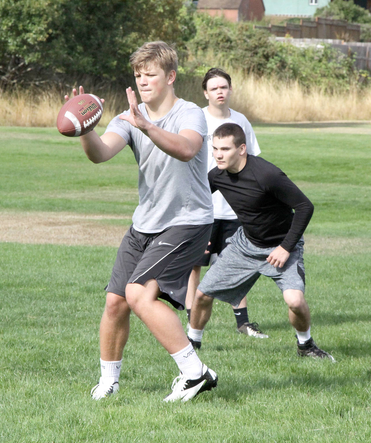 Dave Logan/for Peninsula Daily News Port Angeles quarterback Brenden Roloson-Hines, front, catches the snap while running back Riley Gale awaits a handoff during the first day of high school football practice Wednesday. The Roughriders had 50 players turn out on day one.