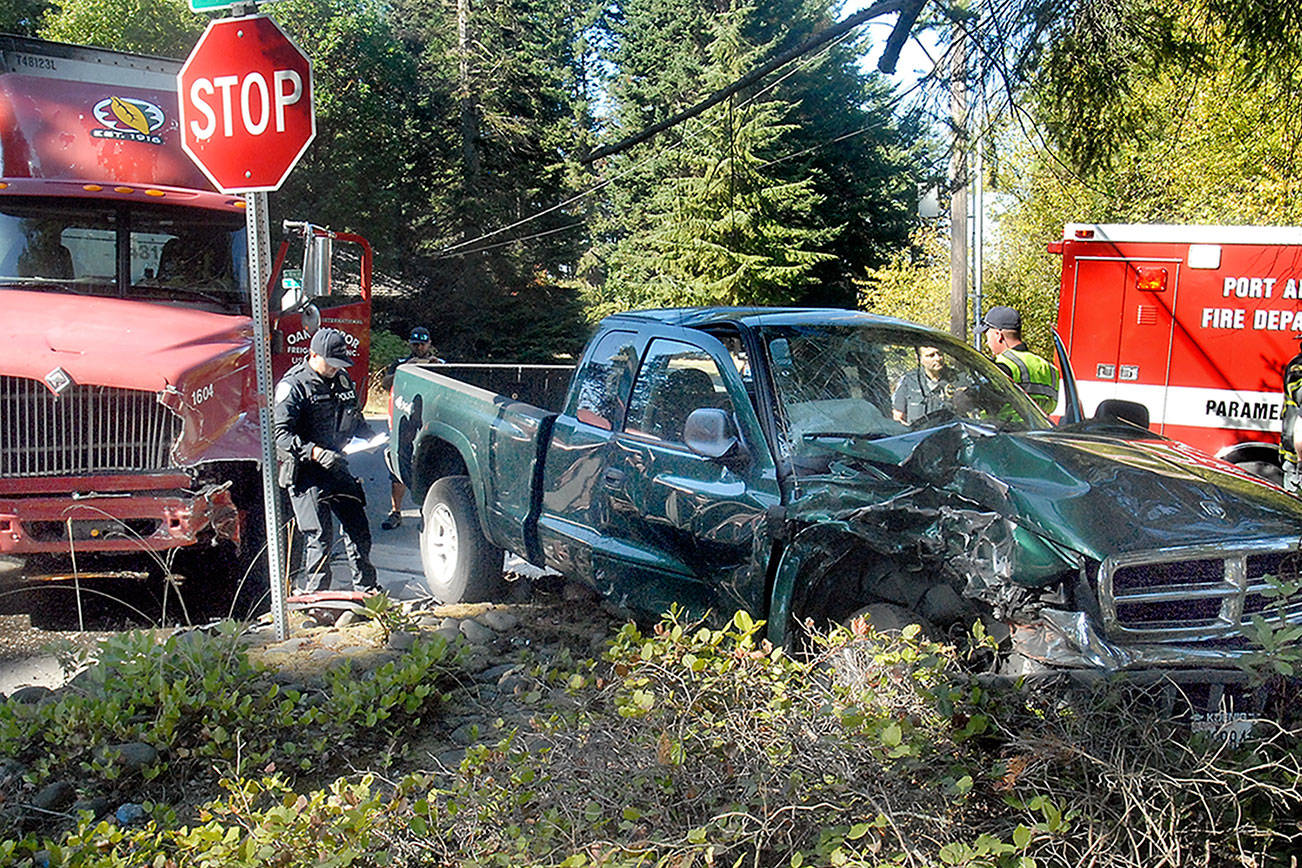 Keith Thorpe/Peninsula Daily News Port Angeles police Officer T.J. Mueller, left, investigates the scene where a pickup truck and a semi-trailer collided at the intersection of 10th and N streets in Port Angeles on Tuesday.