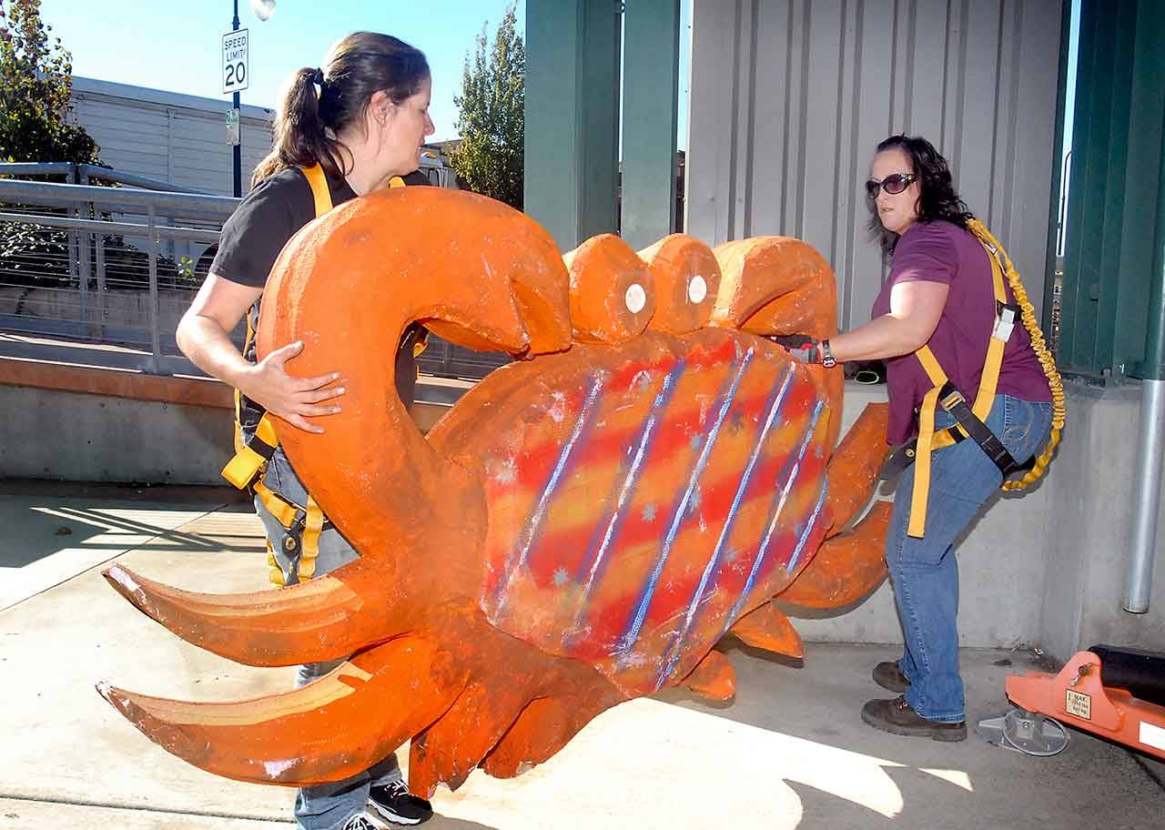 Dungeness Crab & Seafood Festival workers Jeanna Geniesse, left, and Amanda Pinell prepare a crab decoration for hoisting onto the clock tower at The Gateway transit center in downtown Port Angeles on Thursday in advance of this weekend’s event. (Keith Thorpe/Peninsula Daily News)