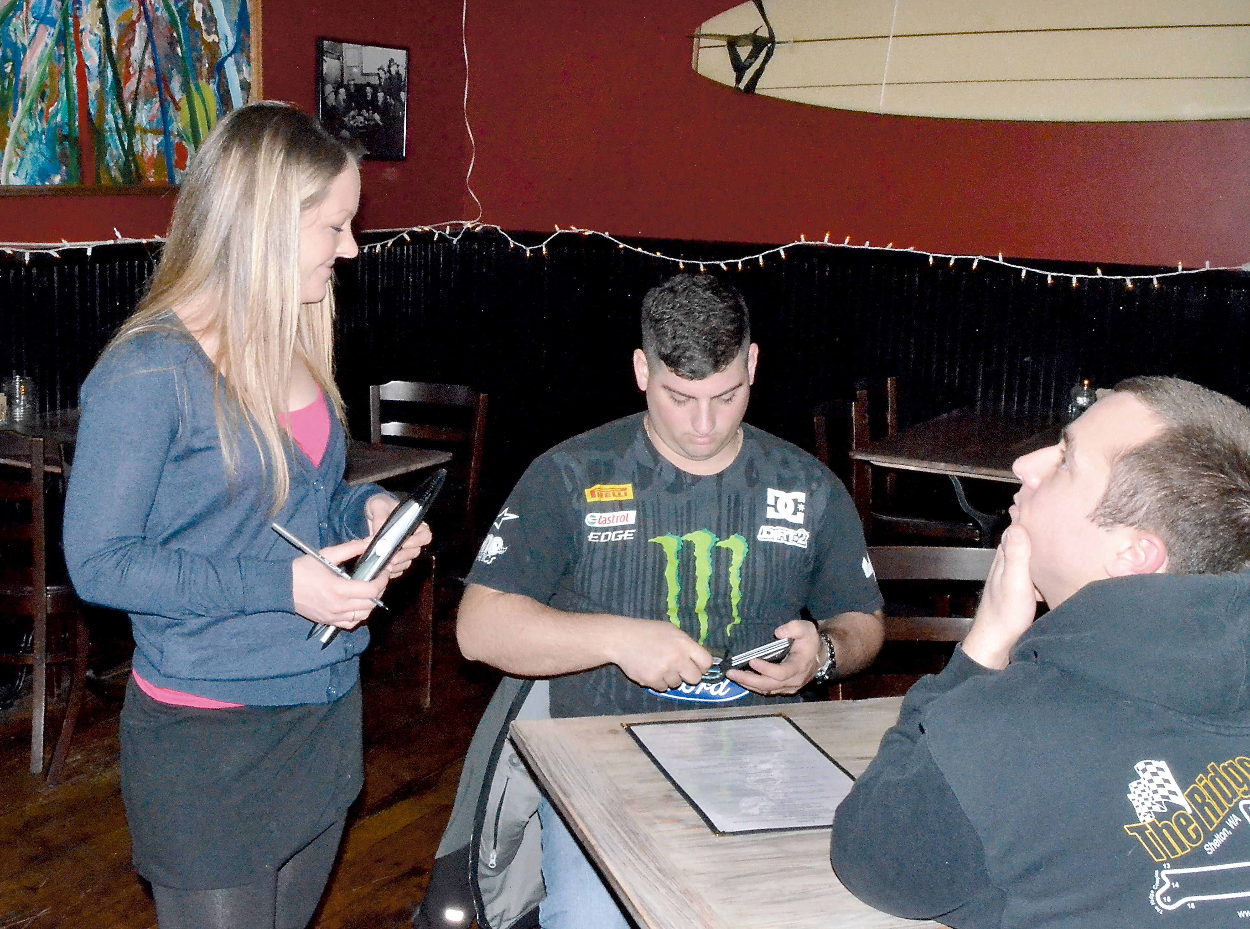 Public House waitress Isabelle Jonland checks ID for USS Stennis crewmember Anthony Lobello. Also pictured is Angelo Cibollaro. (Charlie Bermant/Peninsula Daily News)