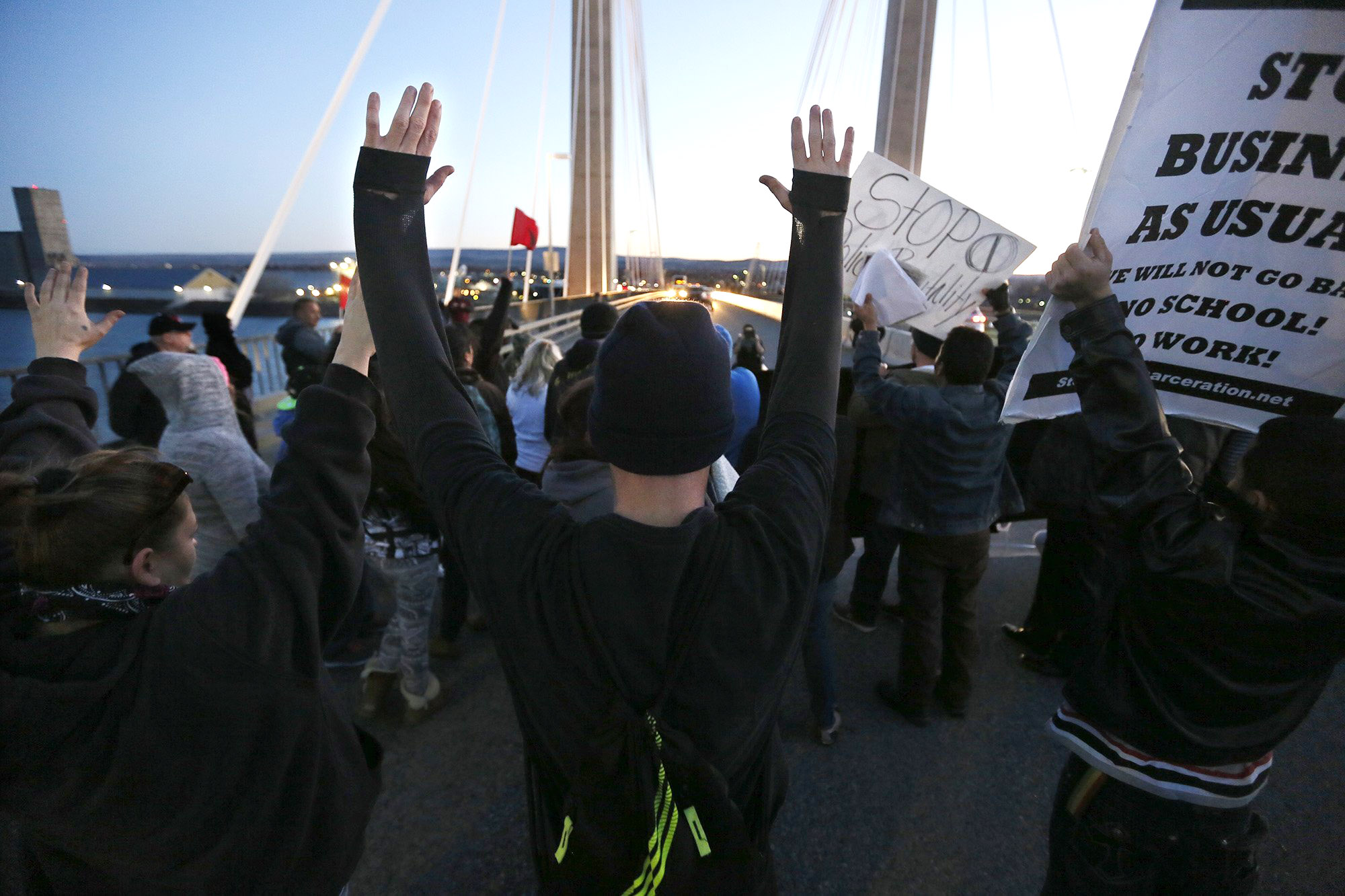 Protesters hold up their hands and signs on a cable bridge in Pasco on Saturday during a protest stemming from the officer-involved shooting death of Antonio Zambrano-Montes. (The Associated Press)