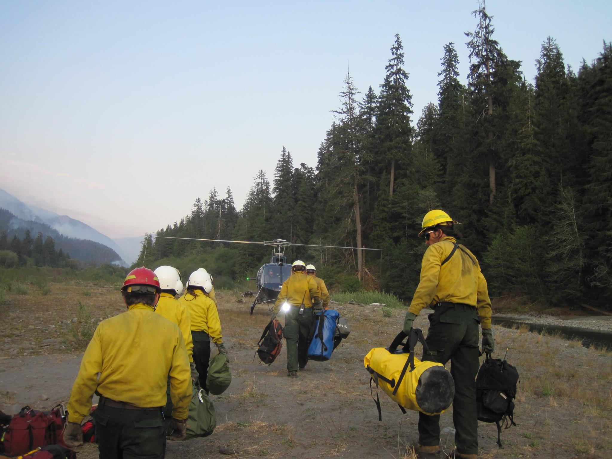 A new shift of firefighters carry their gear to a helicopter on the way to relieve another crew of firefighters at the Paradise Fire area Monday. Olympic National Park