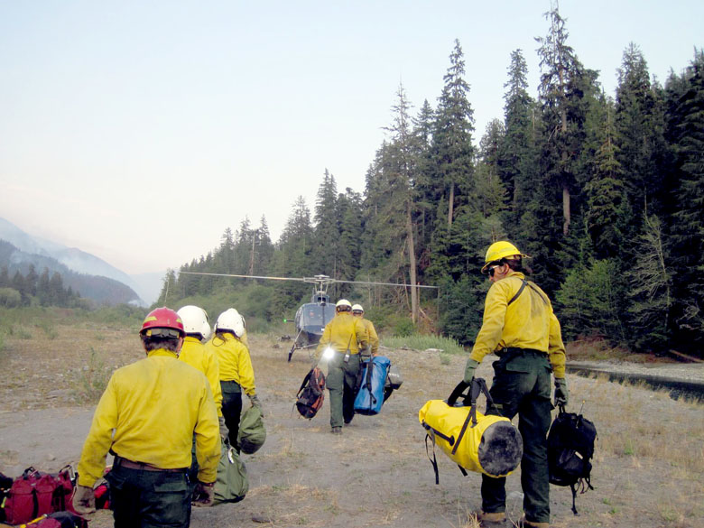 A new shift of firefighters carry their gear to a helicopter on the way to relieve another crew of firefighters at the Paradise Fire area Monday. Olympic National Park