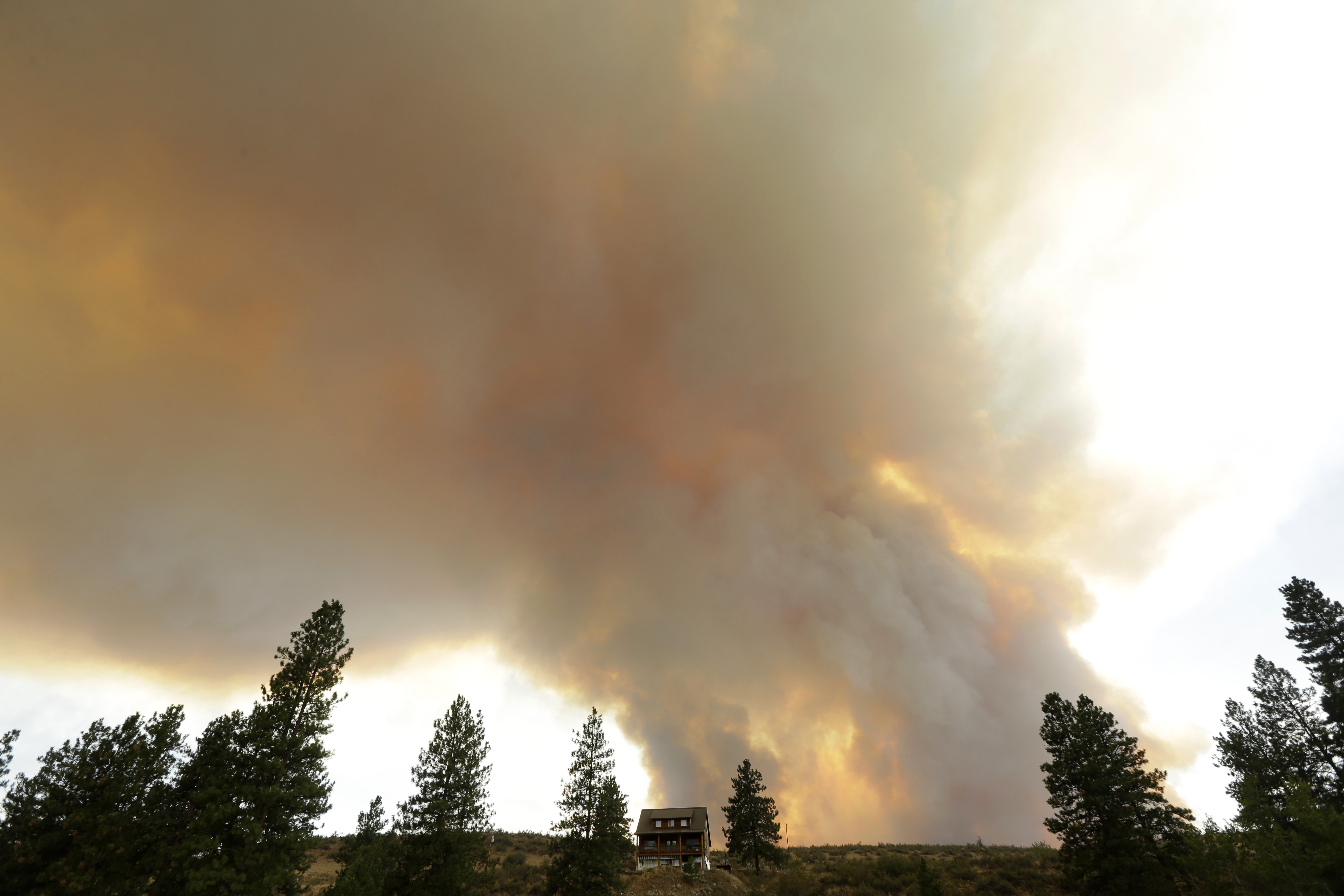 Smoke from an approaching wildfire looms over a home near Twisp on Wednesday. The Associated Press