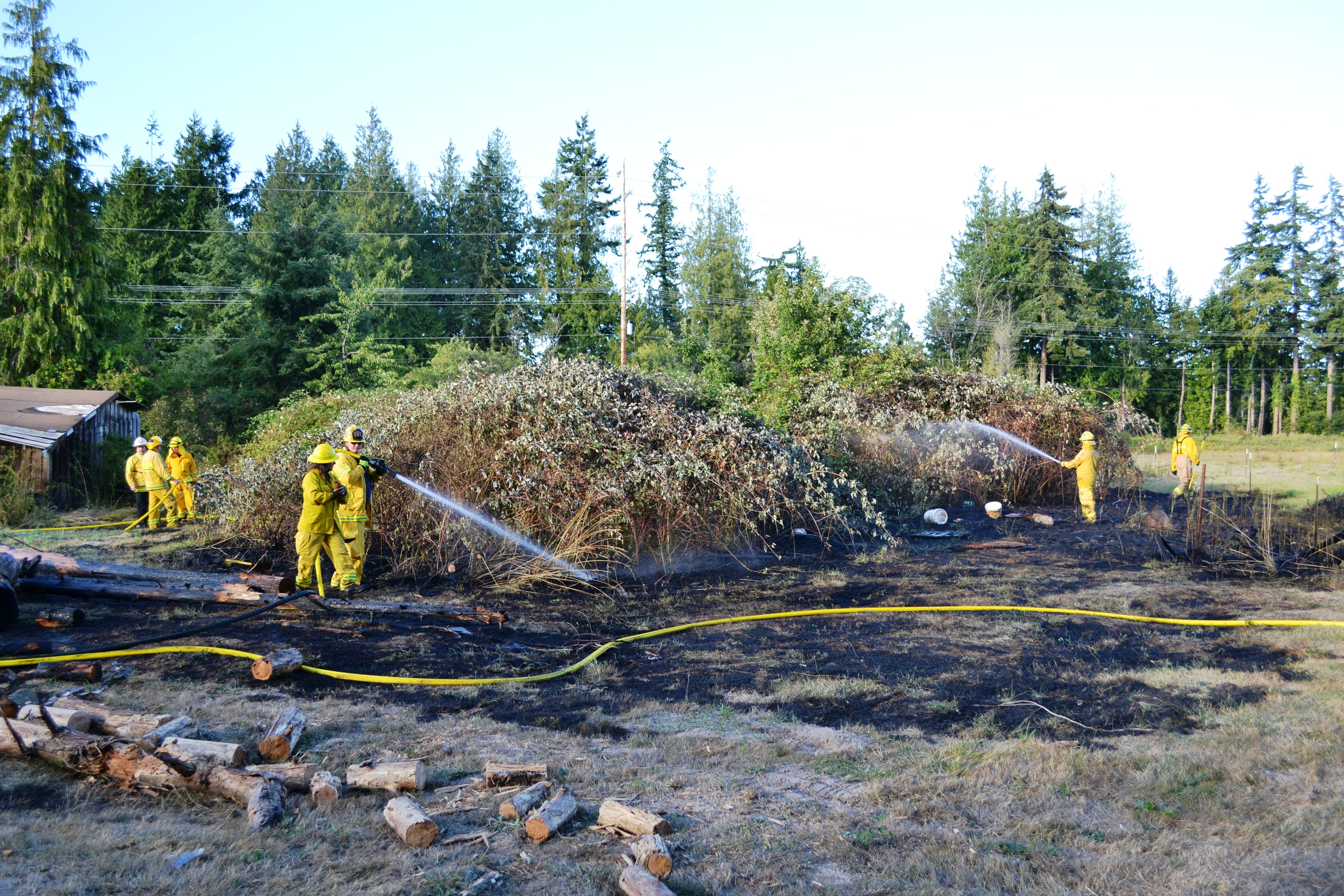 Firefighters with East Jefferson Fire-Rescue and Naval Magazine Indian Island spray down hot spots after extinguishing a brush fire in the 800 block of Four Corners Road in Jefferson County on Sunday. East Jefferson Fire-Rescue