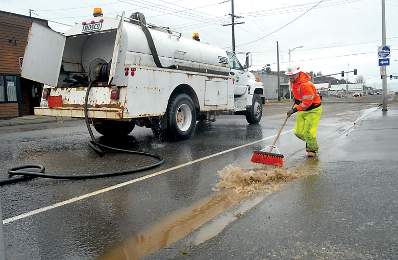 Port Angeles public utility worker Greg Haskins pushes muddy water down a gutter Tuesday on Marine Drive near Cedar Street while cleaning up after a water main break. Keith Thorpe/Peninsula Daily News