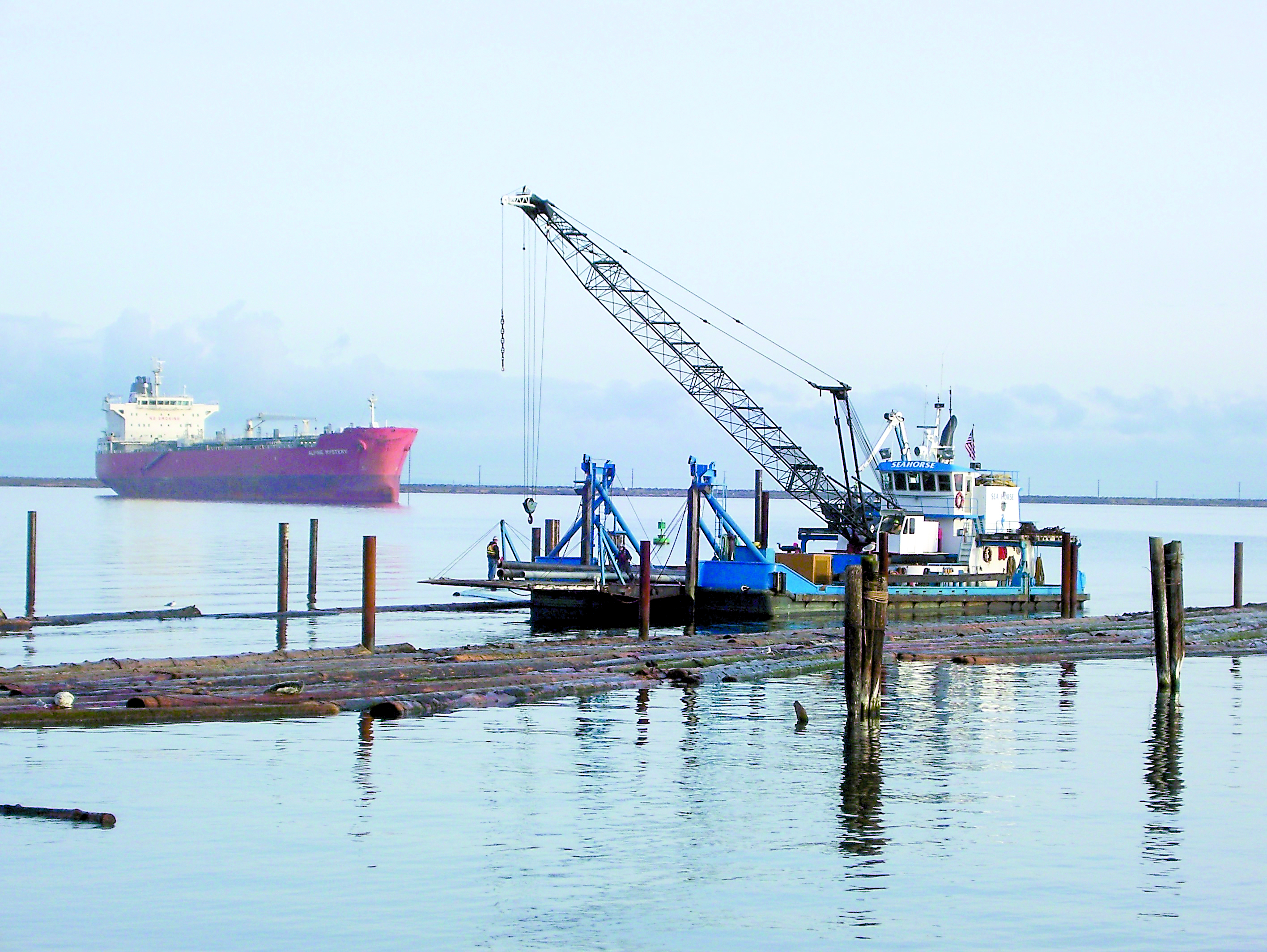 The floating derrick Sea Horse works amid the log booms in Port Angeles Harbor near the Boat Haven breakwater. That’s the oil tanker Alpine Mystery anchored in the harbor at left. -- Photo by David G. Sellars/for Peninsula Daily News