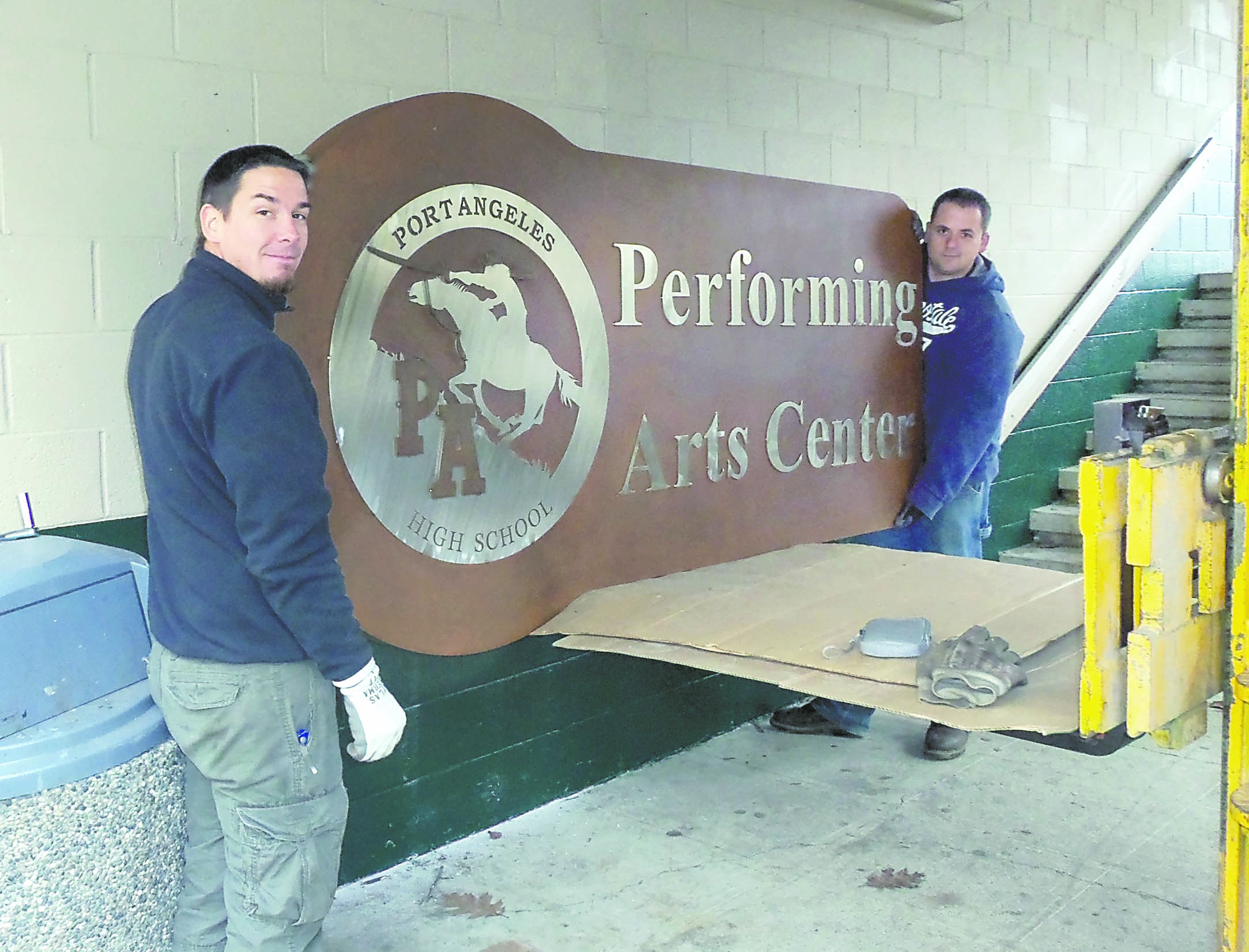 Port Angeles High School maintenance staffers Josh Winters and Jon Keywood install a new sign on the north wall of the auditorium. Port Angeles School District