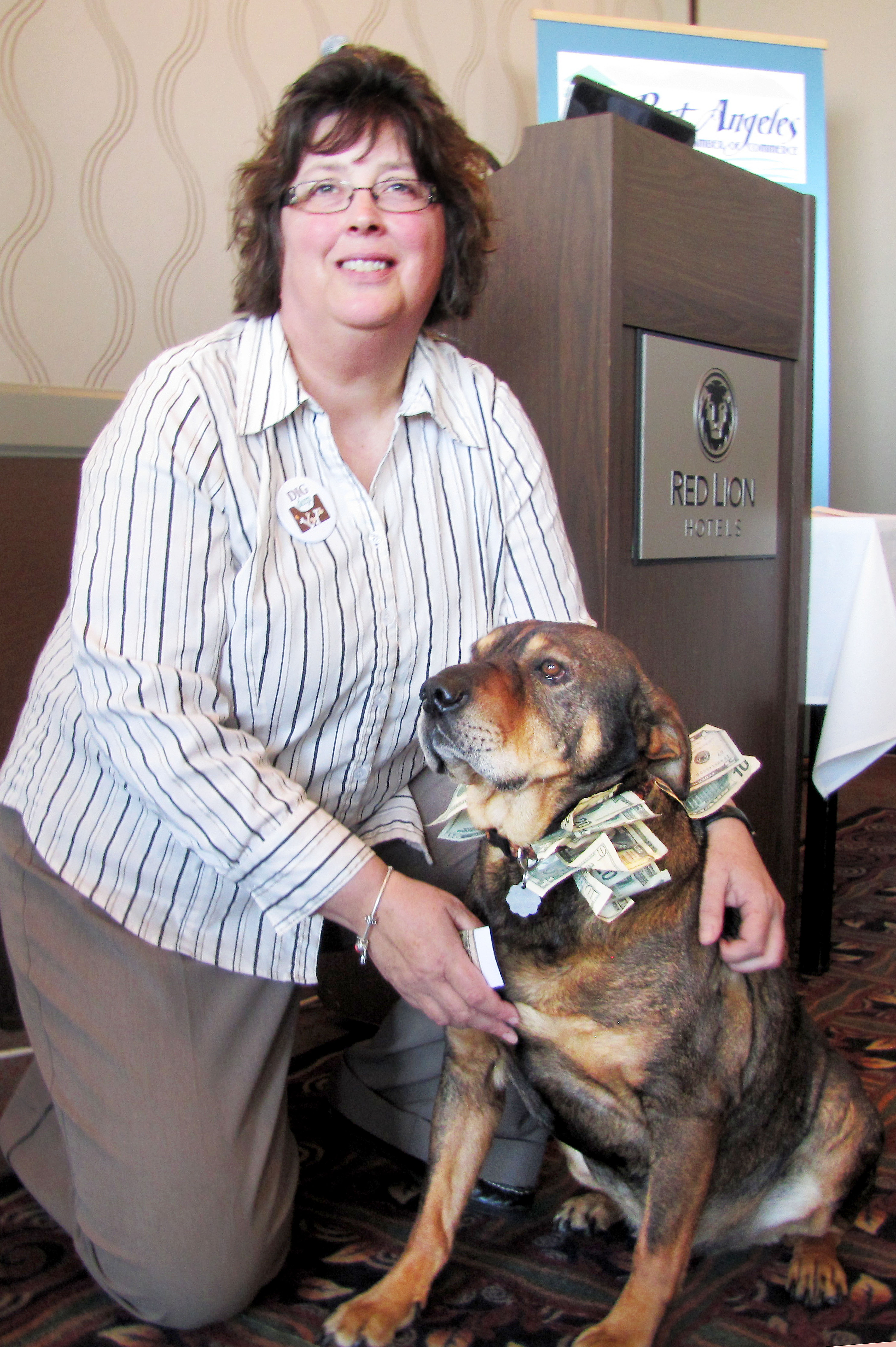 Olympic Peninsula Humane Society Executive Director Mary Beth Wegener and her Buddy the Ambassadog show off the donations Buddy collected while wandering among the Port Angeles Regional Chamber of Commerce audience Monday. Arwyn Rice/Peninsula Daily News