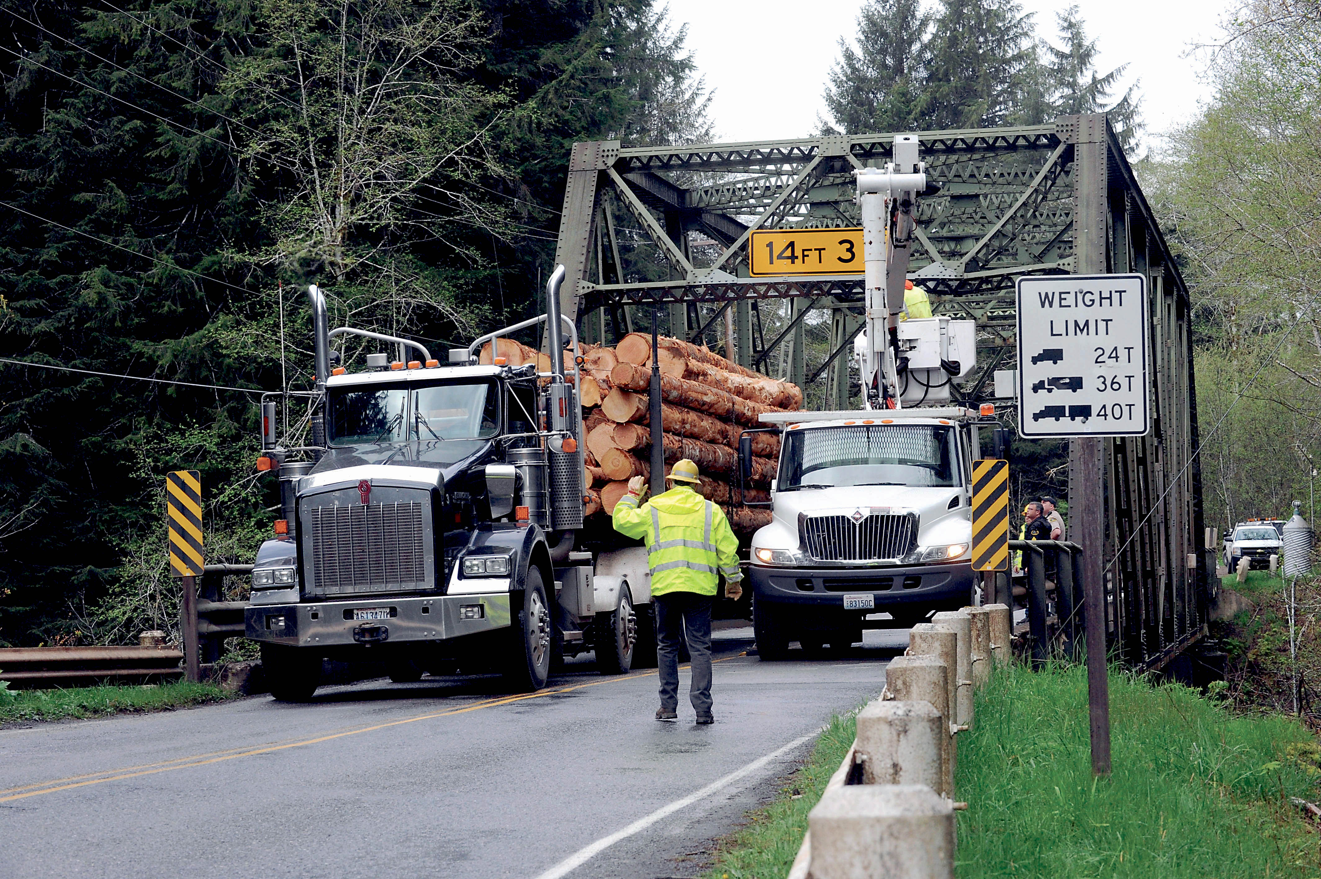 A Clallam County Road Department worker guides a log truck across the Sol Duc River bridge on Quillayute Airport Road on Tuesday as others repair the steel-truss structure.  —Photo by Lonnie Archibald/for Peninsula Daily News