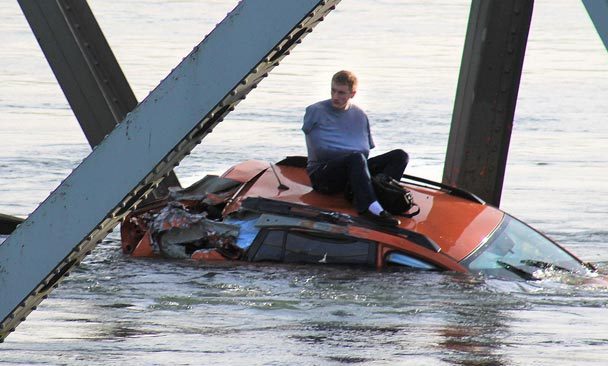 Bryce Kenning waits on the roof of his car for rescuers Thursday evening after it nose-dived from the crumbling Interstate 5 bridge into the Skagit River. The Associated Press