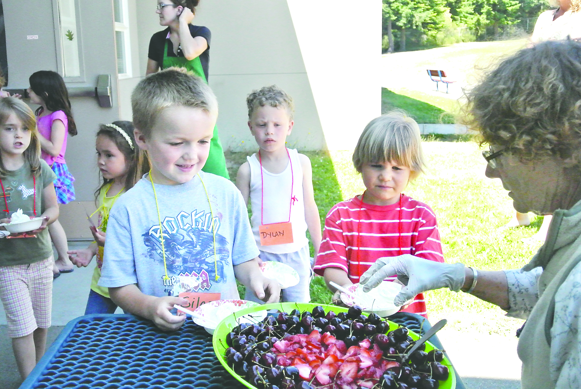 Volunteer Eliana Rose dishes out cherries and strawberries at an ice-cream social at Chimacum Creek Primary School on Wednesday. Kids taking part in the event include Silas Cotton