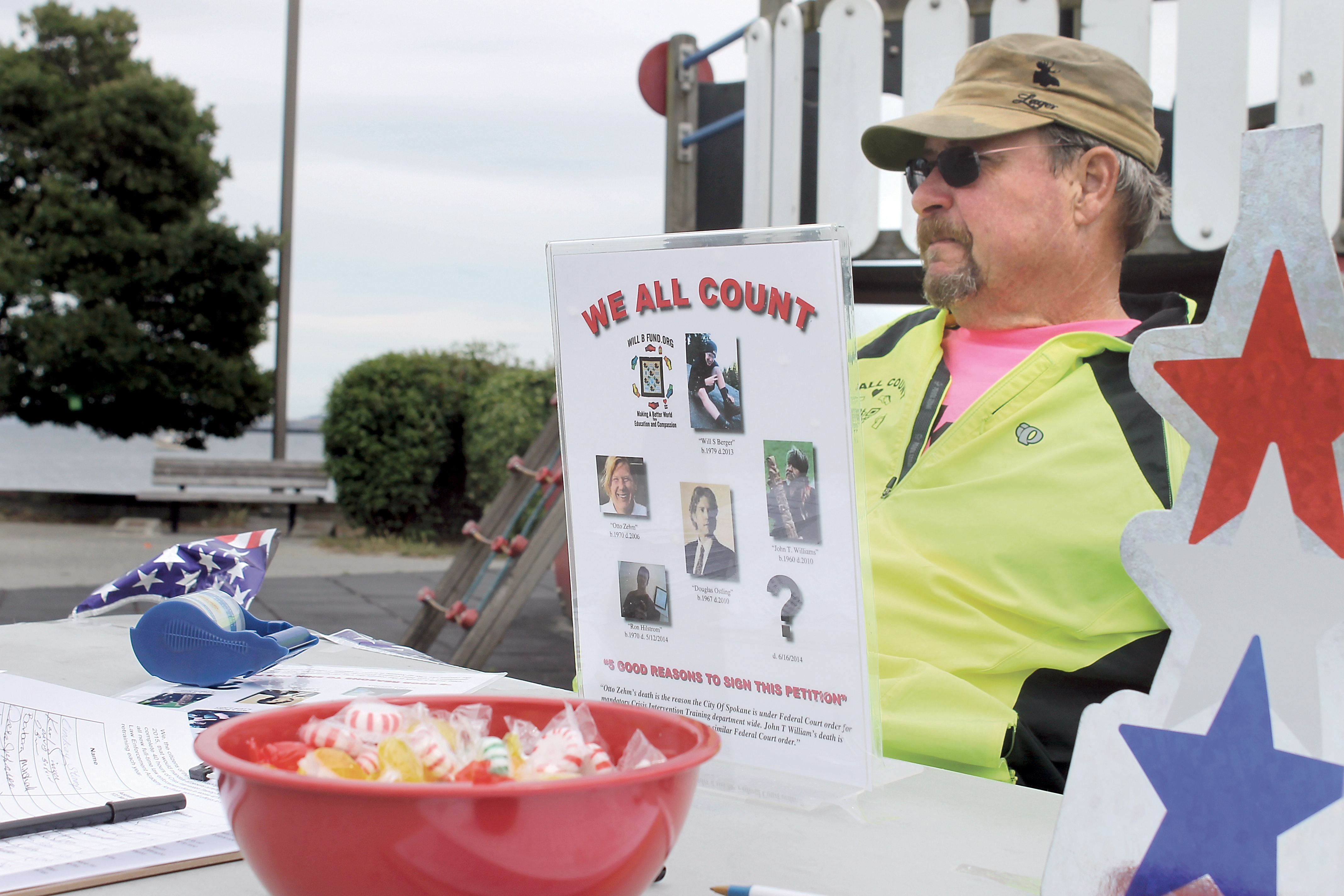 Bill Berger sits at a table he and friends and family set up at Port Angeles City Pier on Friday afternoon to distribute information about the importance of crisis-intervention training for law enforcement officers. —Photo by Jeremy Schwartz/Peninsula Daily News