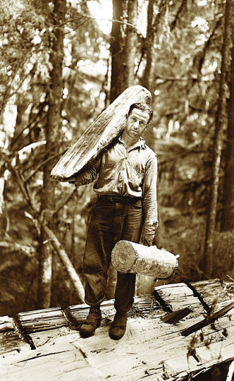 A logger wearing a hickory shirt stands atop a felled tree in this vintage photo. Hickory Shirt/Heritage Days celebrates Forks' logging traditions. Forks Timber Museum