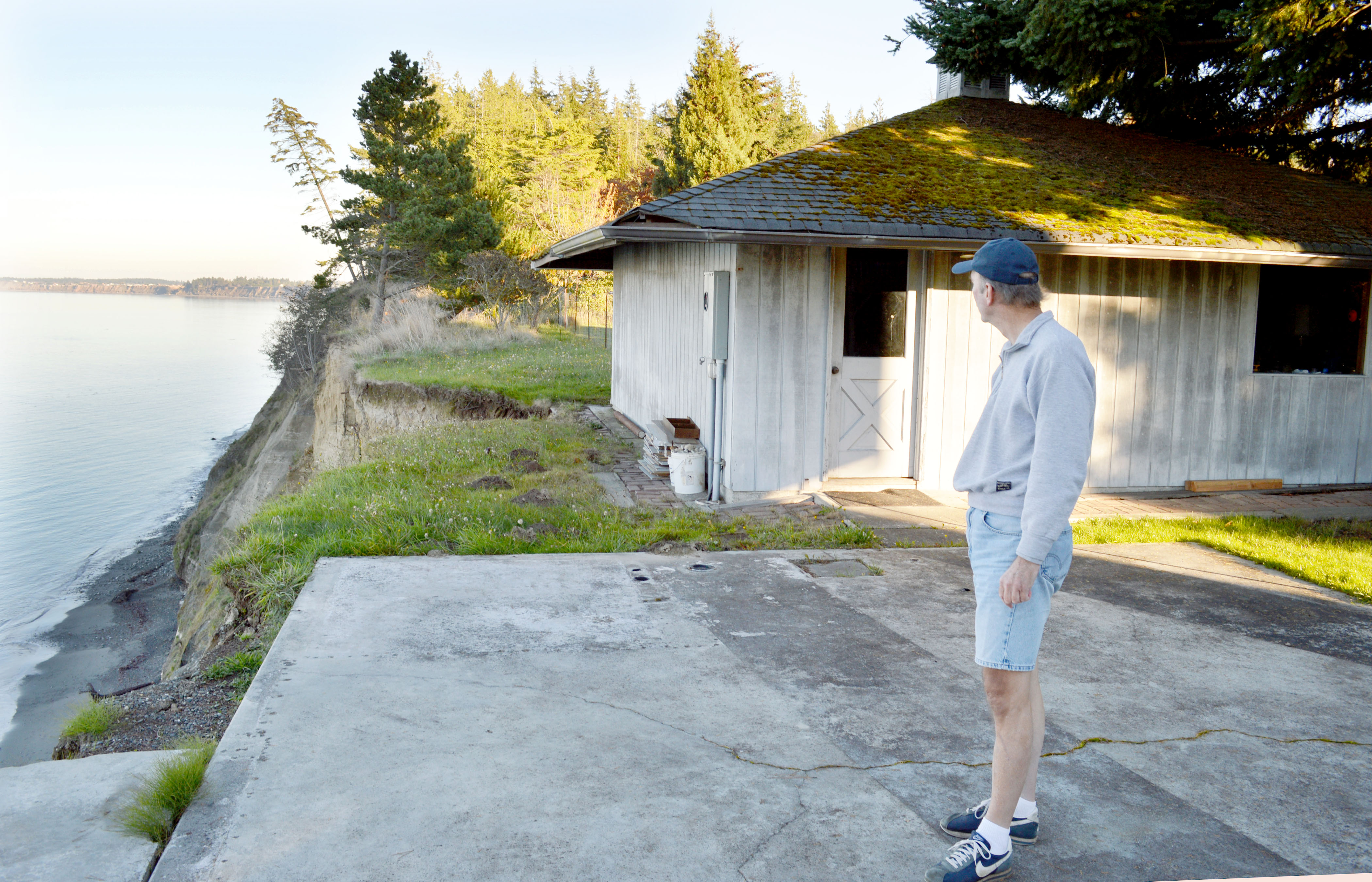 Tim Smith looks at the bluff that broke off behind the garage of his home on Gehrke Road in a July landslide. Smith said erosion has taken away a good portion of his backyard over the past several years.  -- Photo by Joe Smillie/Peninsula Daily News