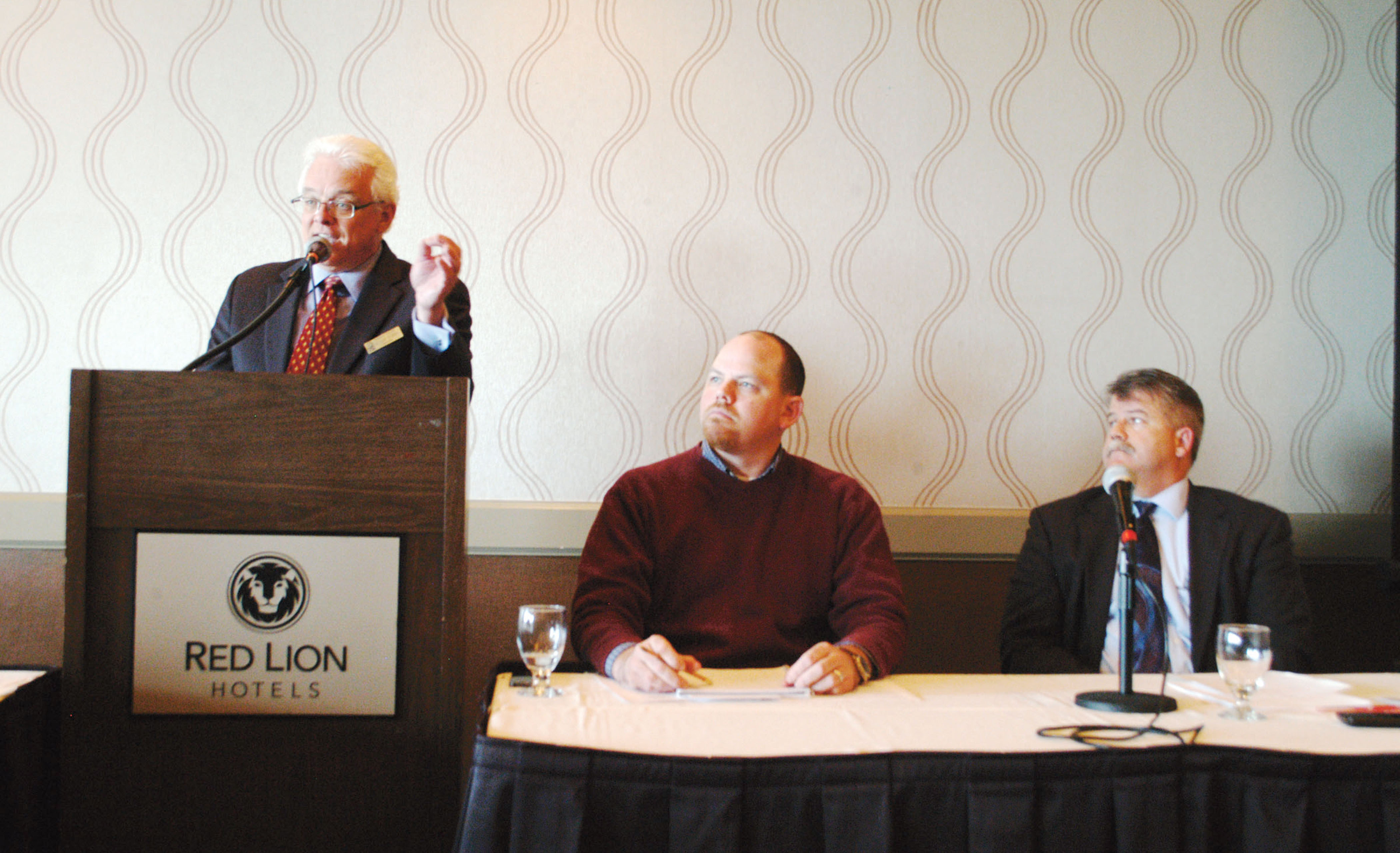 Peninsula College President Luke Robins addresses the Port Angeles Regional Chamber of Commerce audience as fellow panelists Brian Kuh