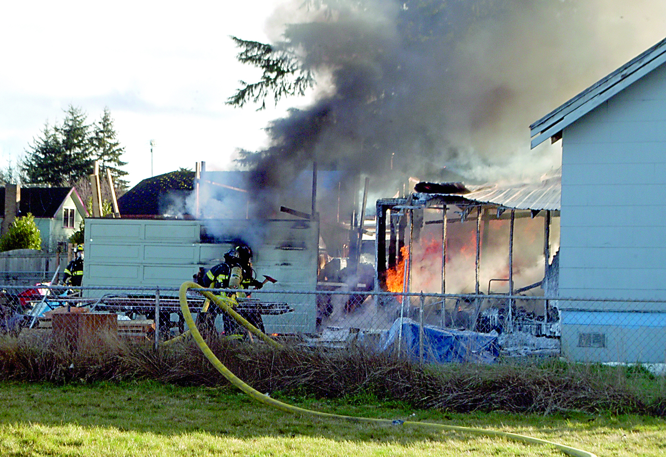 Firefighters with the Port Angeles Fire Department work to extinguish a blaze that burned through an out building next to a home along North Liberty Street between Front and Georgiana streets Saturday morning.  —Photo by Jeremy Schwartz/Peninsula Daily News