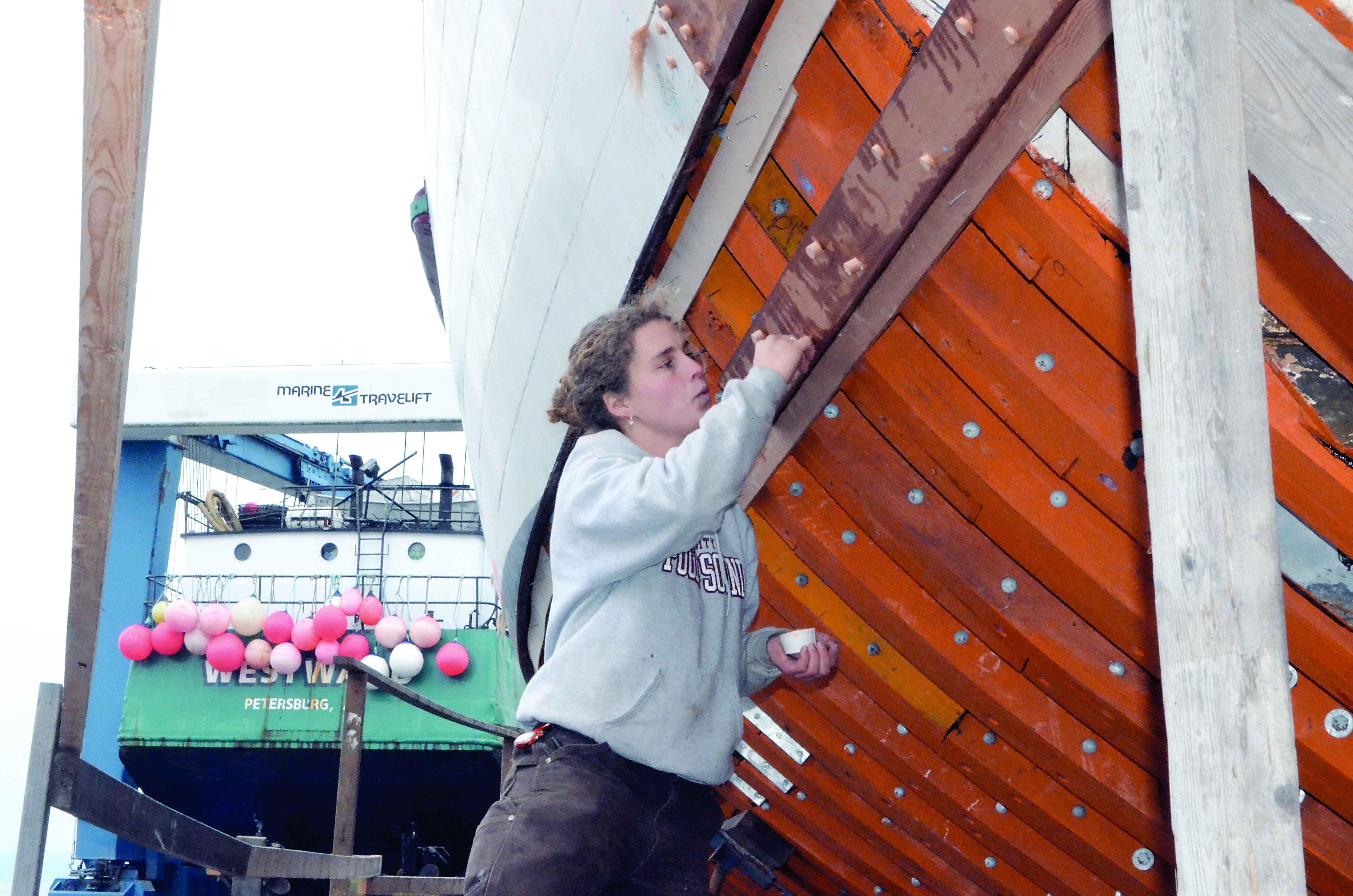 Volunteer Alea Robertson taps “bungs” — used to smooth over holes left by fasteners that bind planks to a vessel — into the hull of the Adventuress. — Charlie Bermant/Peninsula Daily News