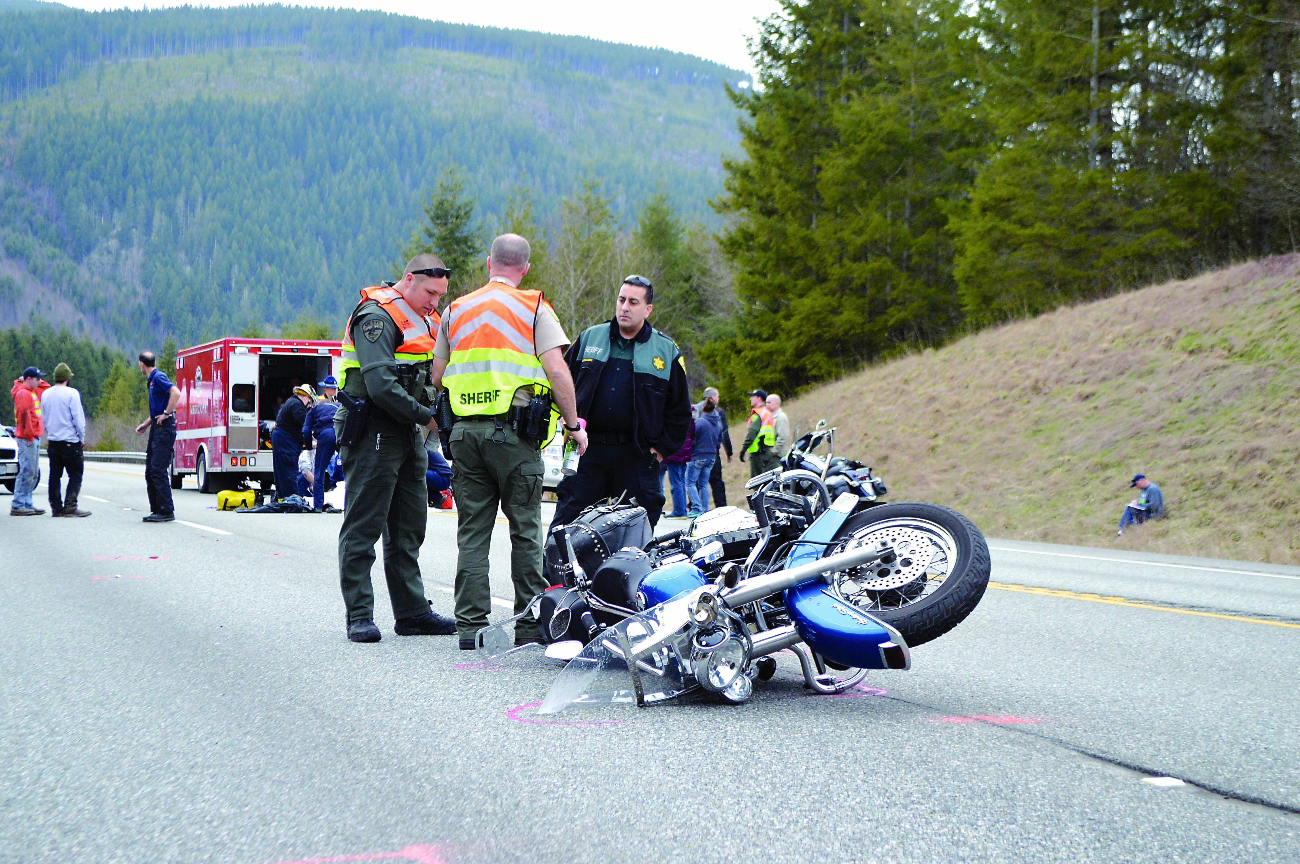 Jefferson County Sheriff Tony Hernandez speaks with Deputies Darren Dotson and Brandon Przygocki at the scene of an accident on state Highway 104 east of the U.S. Highway 101 junction. The crash sent the rider of this motorcycle to Harborview Medical Center in Seattle on Thursday afternoon. — Joe Smilie/Peninsula Daily News