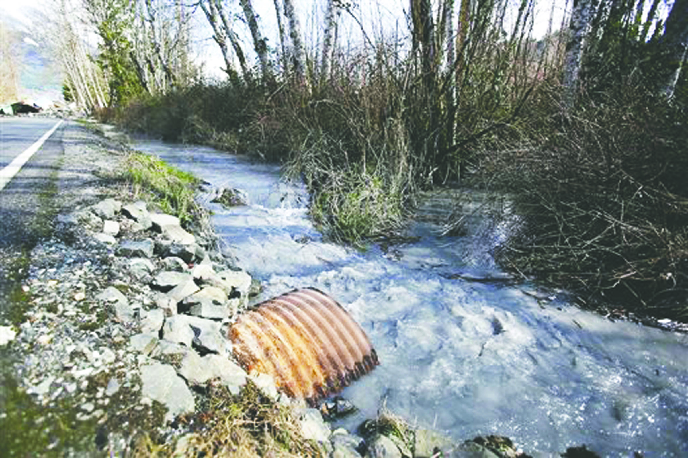 A steady stream of mud and water flows away from the mudslide blocking the road on state Highway 530 on Sunday