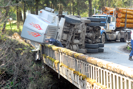 Port Angeles Police Cpl. Tom Kuch peers over the edge of the bridge over U.S. Highway 101 from the Tumwater Truck Route — state Highway 117 — after a log truck overturned negotiating the turn. Keith Thorpe/Peninsula Daily News