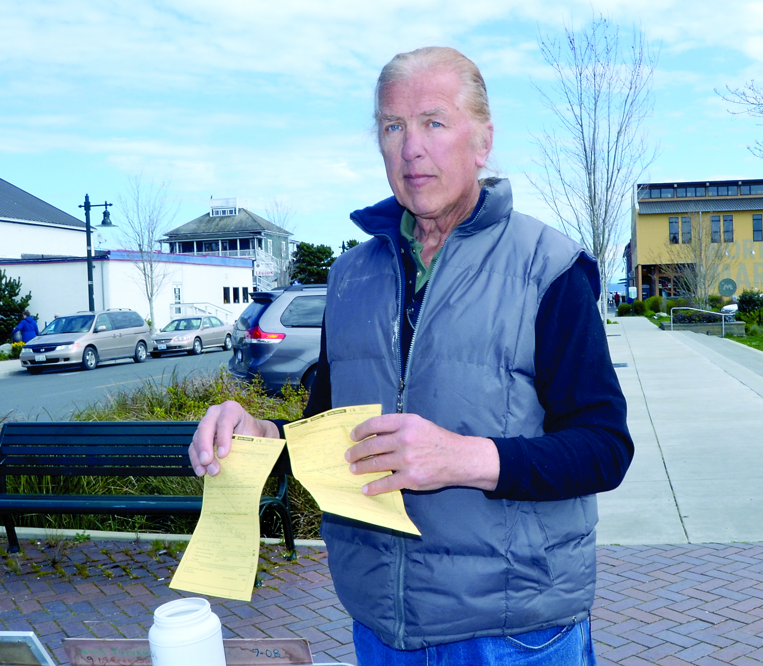 Richard Erik Olson displays the two summons he received Monday for being out of compliance with the city of Port Townsend’s recently approved sign code. — Charlie Bermant/Peninsula Daily News