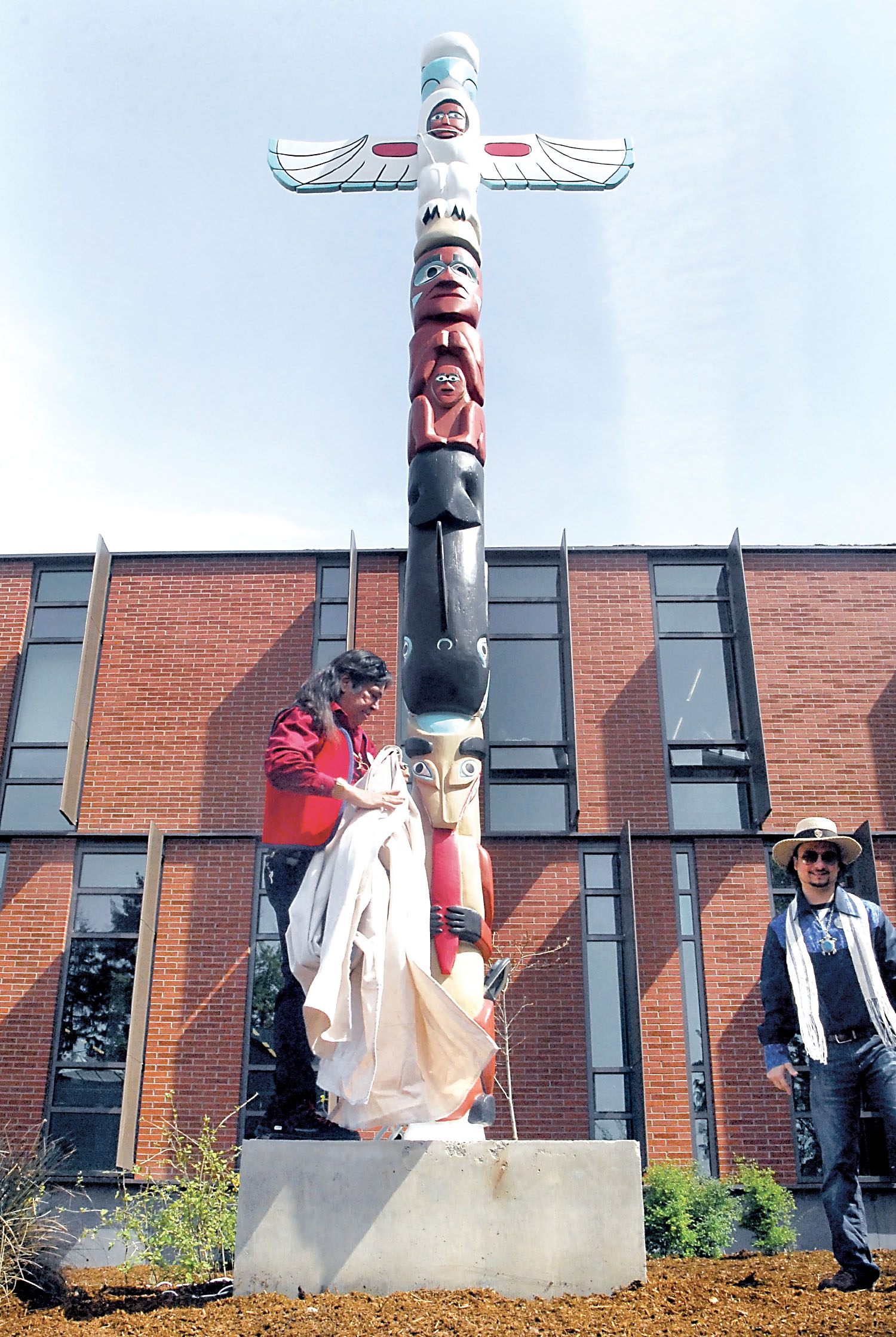 Totem pole restorer Terry Johnson pulls the cover from a totem pole during Tuesday’s unveiling ceremony near the Maier Hall on the Port Angeles campus of Peninsula College. — Keith Thorpe/Peninsula Daily News