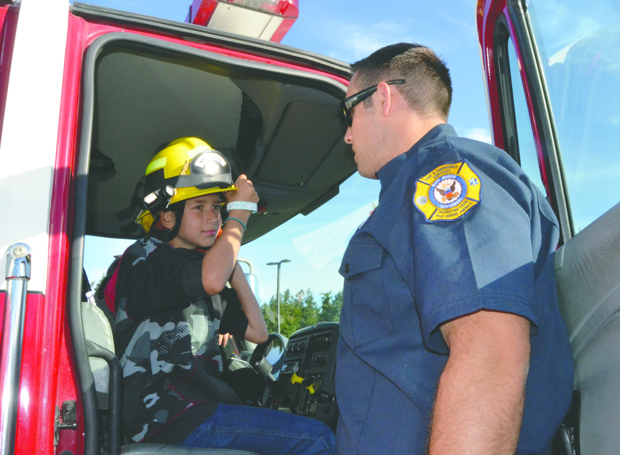 Chimacum Middle School student Dawson Paden tries on a fireman's hat Thursday with firefighter Matt Millich of Naval Magazine Indian Island. Charlie Bermant/Peninsula Daily News