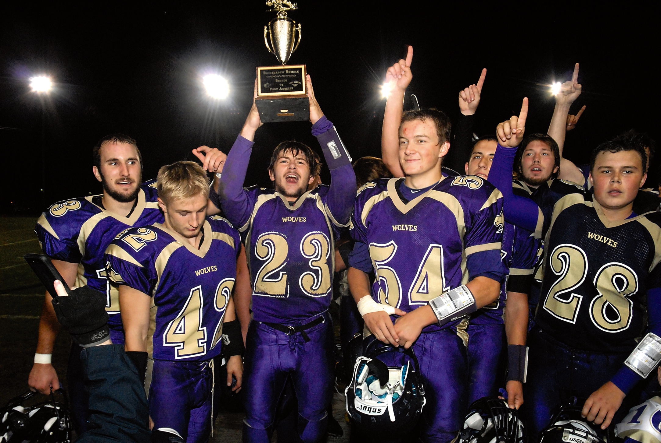 Gavin Velarde (23) holds up the Rainshadow Rumble trophy after Sequim defeated Port Angeles 49-6. Among those joining in the celebration were