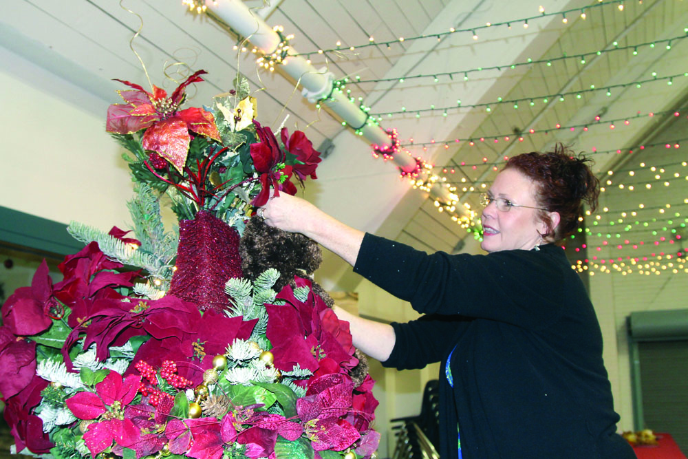 Rhonda Raymond of Port Angeles adjusts the top of a tree called “Victorian Charm” as she and dozens of other designers make last minute adjustments for the Festival of Trees in the Vern Burton Community Center this weekend. Dave Logan/for Peninsula Daily News