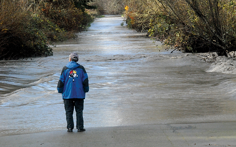 Lower Elwha Klallam tribal member Ben Charles Sr. looks over a rain-swollen Elwha River after it left its banks and spread out over Lower Elwha Road on the Lower Elwha Klallam reservation west of Port Angeles on Wednesday. Keith Thorpe/Peninsula Daily News