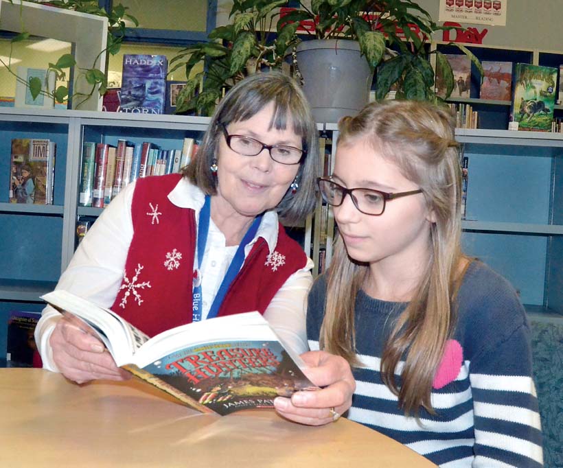 Blue Heron Middle School Librarian Cheryl Brady examines a book by James Patterson with her grandchild Ava Brady