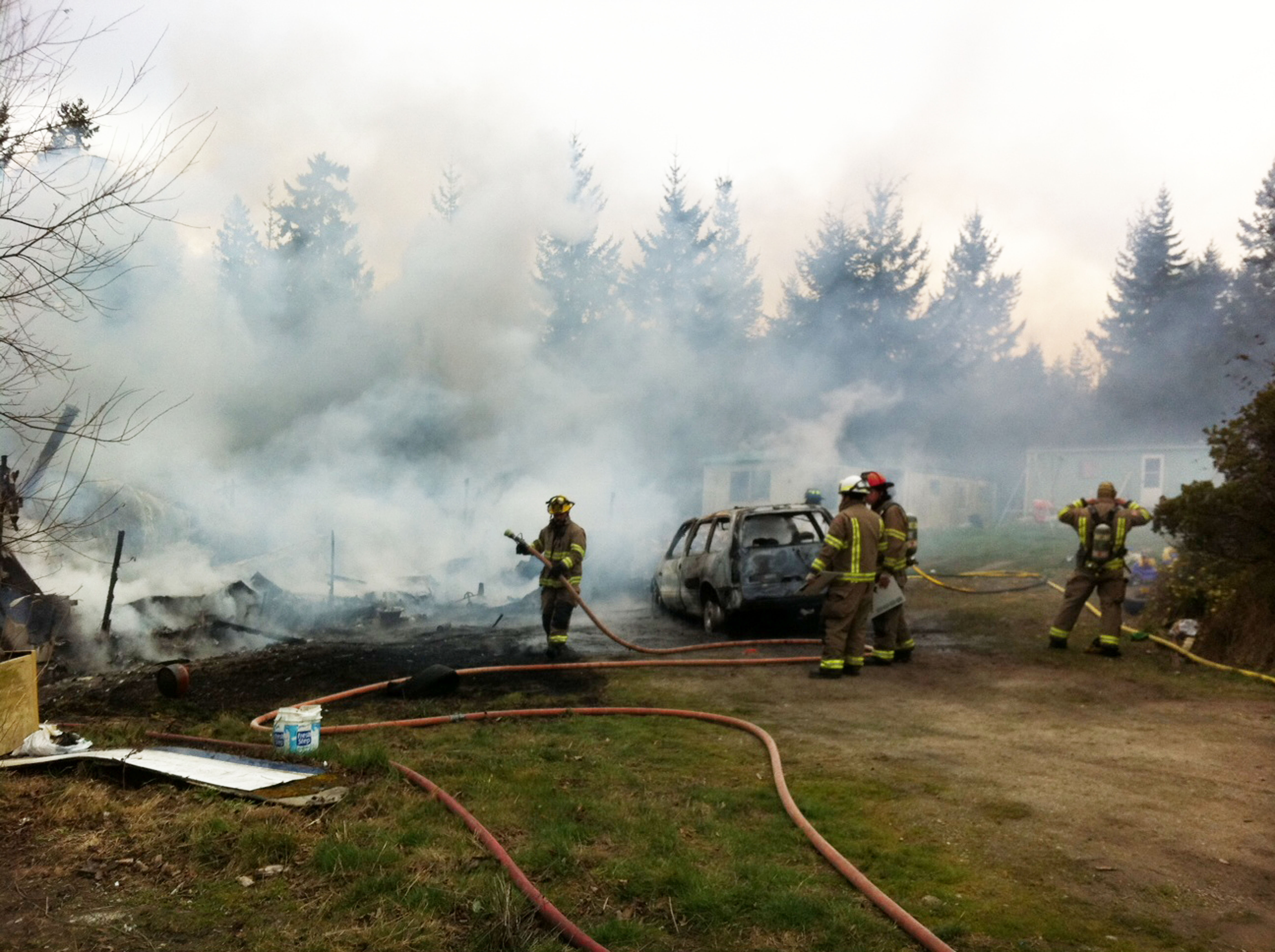 The remains of a mobile home in Diamond Point are tended to by Clallam County Fire District No. 3 firefighters. Jeff Chew/Peninsula Daily News