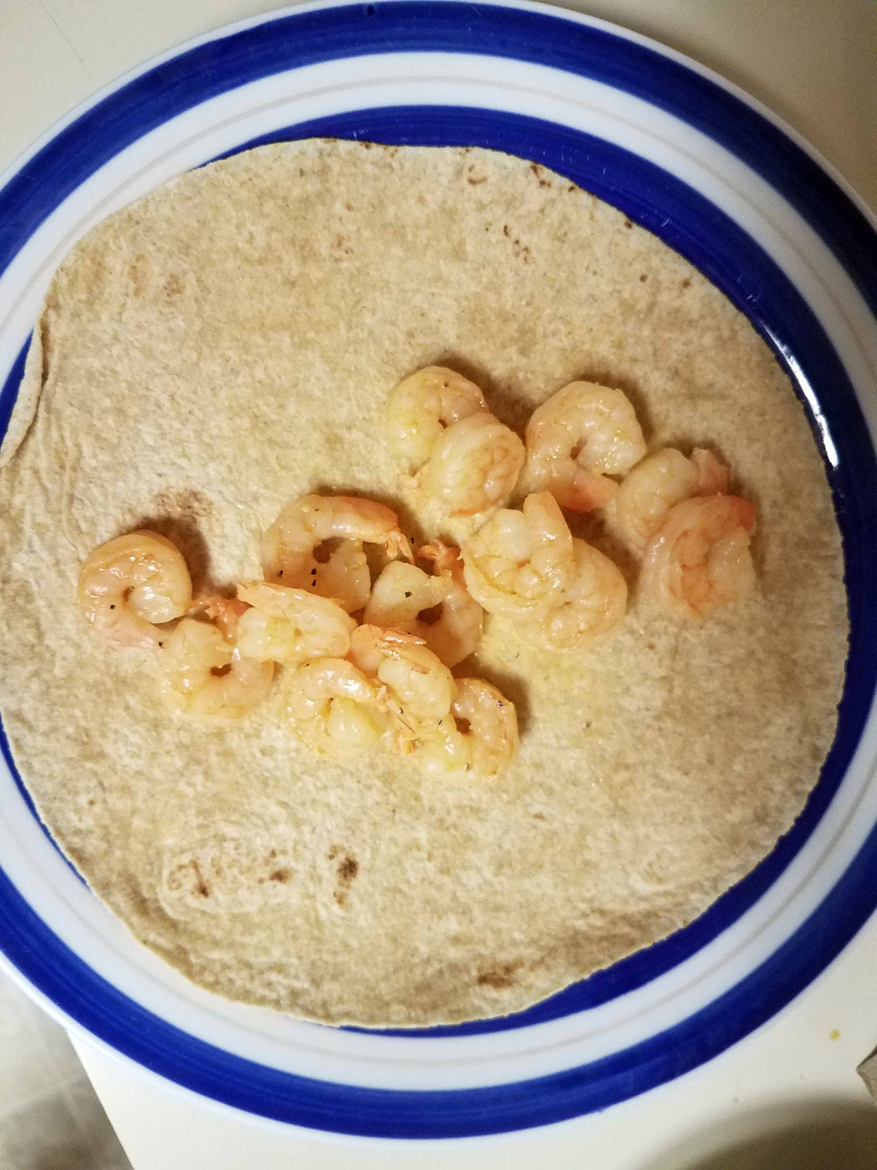 Mexican shrimp rest on a whole wheat tortilla, awaiting cheese and other burrito ingredients. (Emily Hanson/Peninsula Daily News)