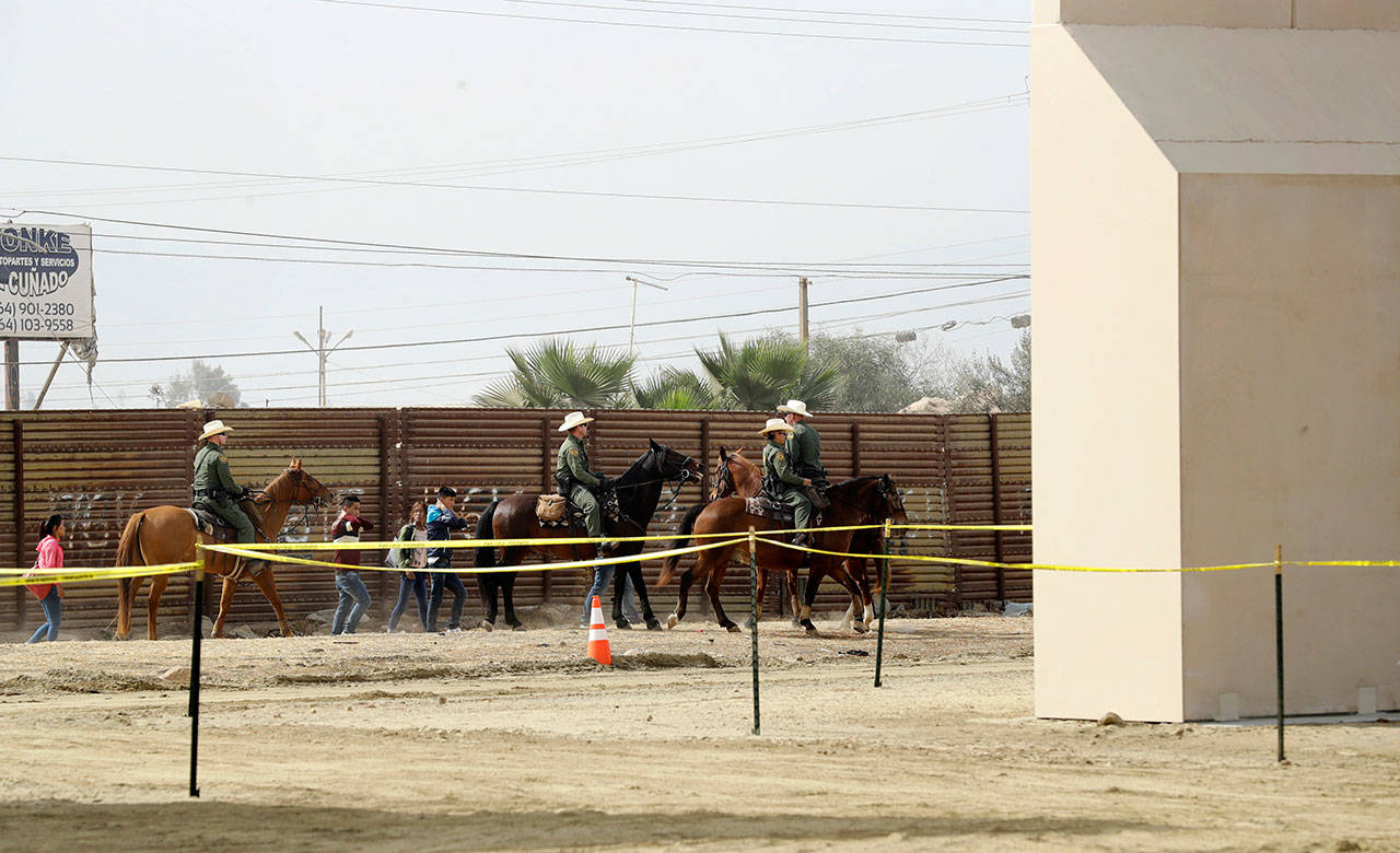 In this Oct. 19, 2017, file photo, a group of people are detained by Border Patrol agents on horseback after crossing the border illegally from Tijuana, Mexico, near where prototypes for a border wall, right, were being constructed in San Diego. (The Associated Press)