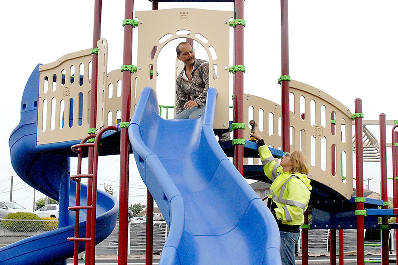 Keith Thorpe/Peninsula Daily News Port Angeles Parks Department worker Brooke Keohokaloke, right, hands a drill to coworker Leon Leonard as the pair assemble new playground equipment at Georgiana Park in Port Angeles on Tuesday. The equipment was the result of $148,000 in funding and in-kind labor to buy new playground pieces and a wheelchair-friendly surface for the play area, located a block from Olympic Medical Center. Keohokaloke said the goal was to have the equipment finished and the playground open by the end of summer.